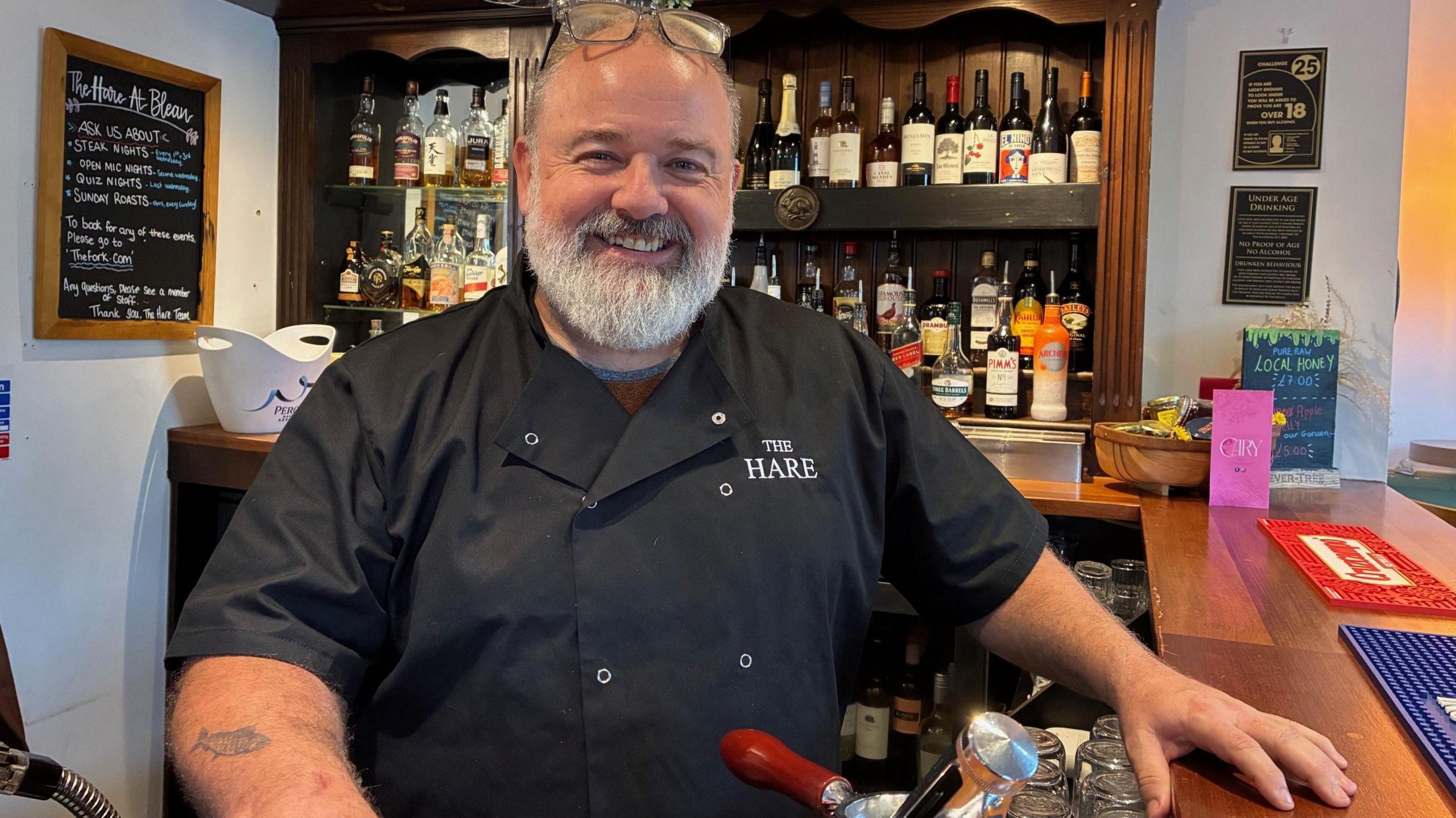 Matthew Hayden stands behind the bar of his pub wearing a chef's top branded with The Hare pub name.