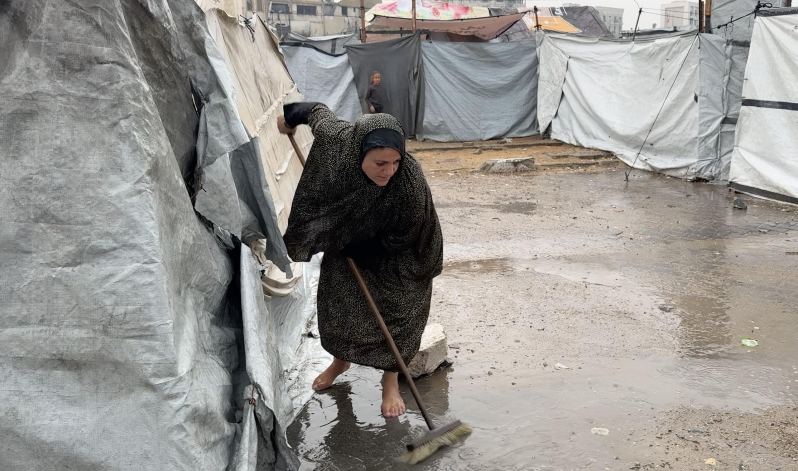A Palestinian woman brushes away water on the ground in front of a tent
