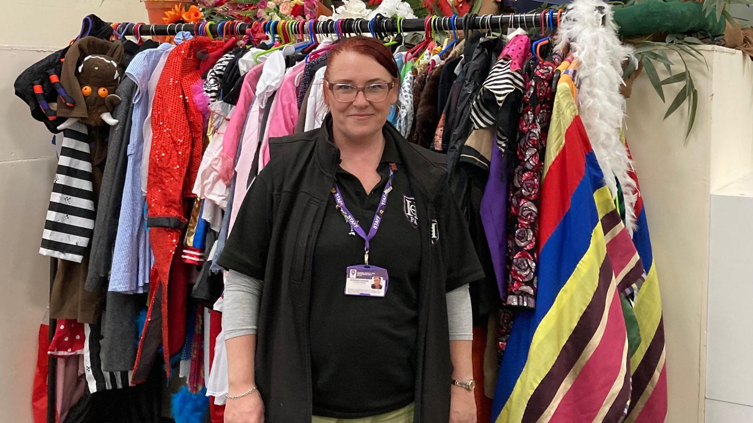 Eleanor 'Elle' Dicks, founder of Haddon Charity of Performing Arts, standing in front of a multi-coloured costume rack. 