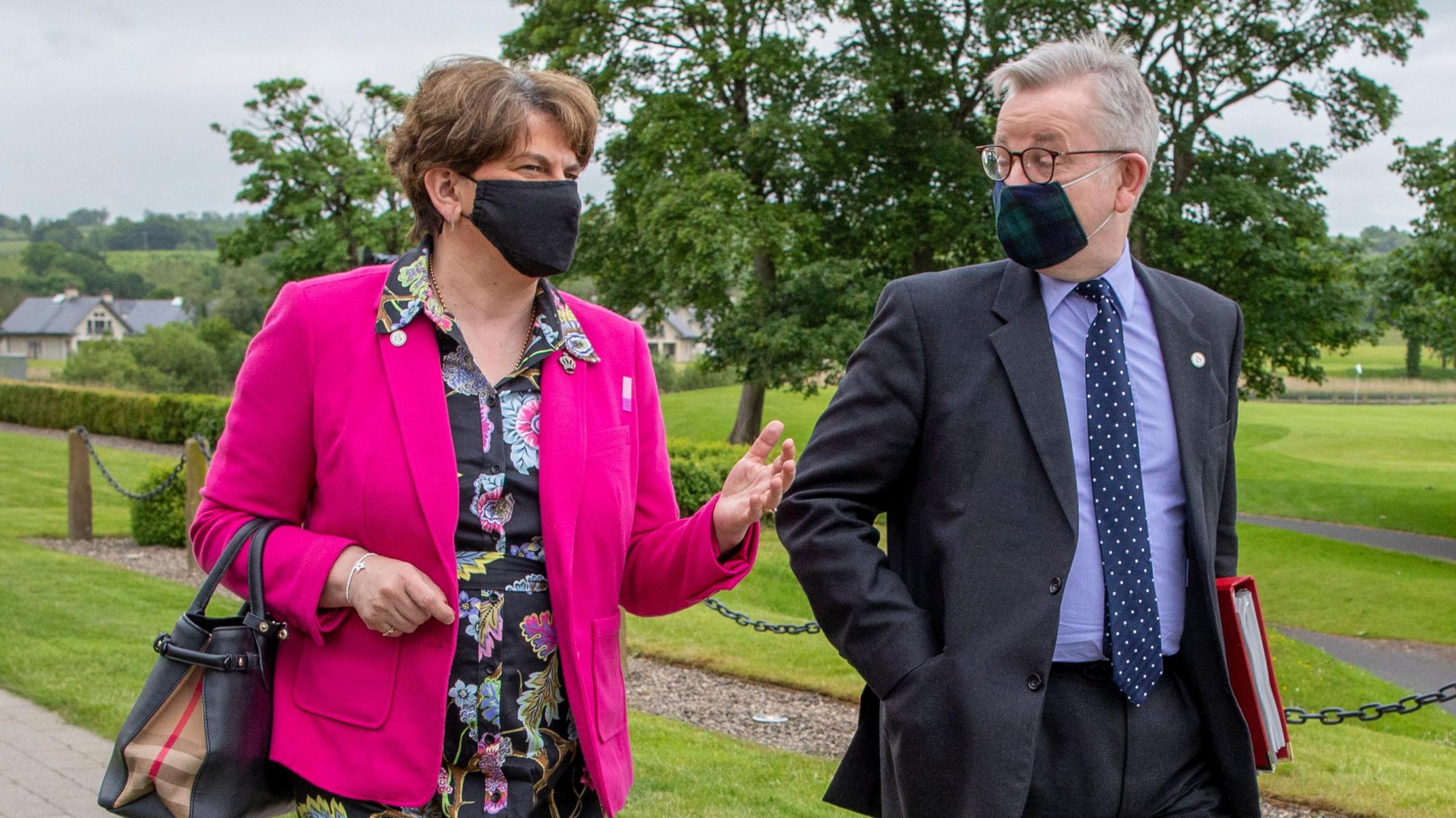 Arlene Foster and Michael Gove arrive for a meeting of the British-Irish Council at the Lough Erne Resort in Enniskillen in June 2021.  She is wearing a pink jacket and black floral dress.  He is wearing a dark blue suit and blue shirt.  Both are wearing black face masks due to the Covid restrictions of the time. 