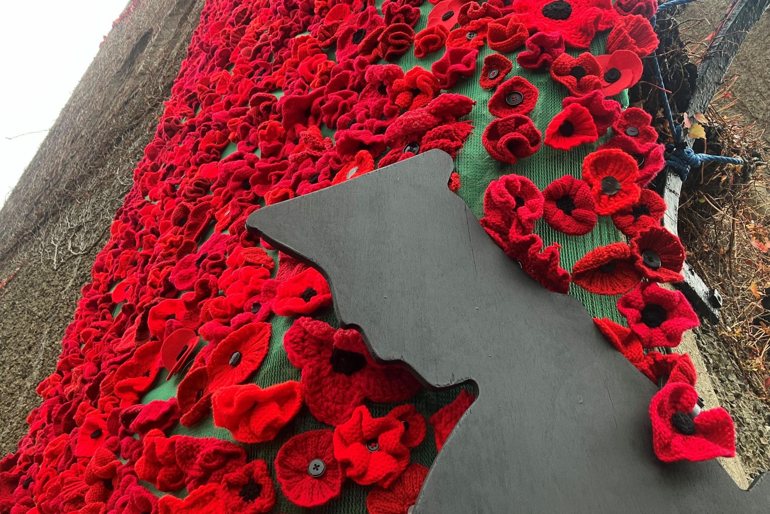 Hand-knitted poppies on the exterior wall of a church, there is also a black silhouette of a soldier.