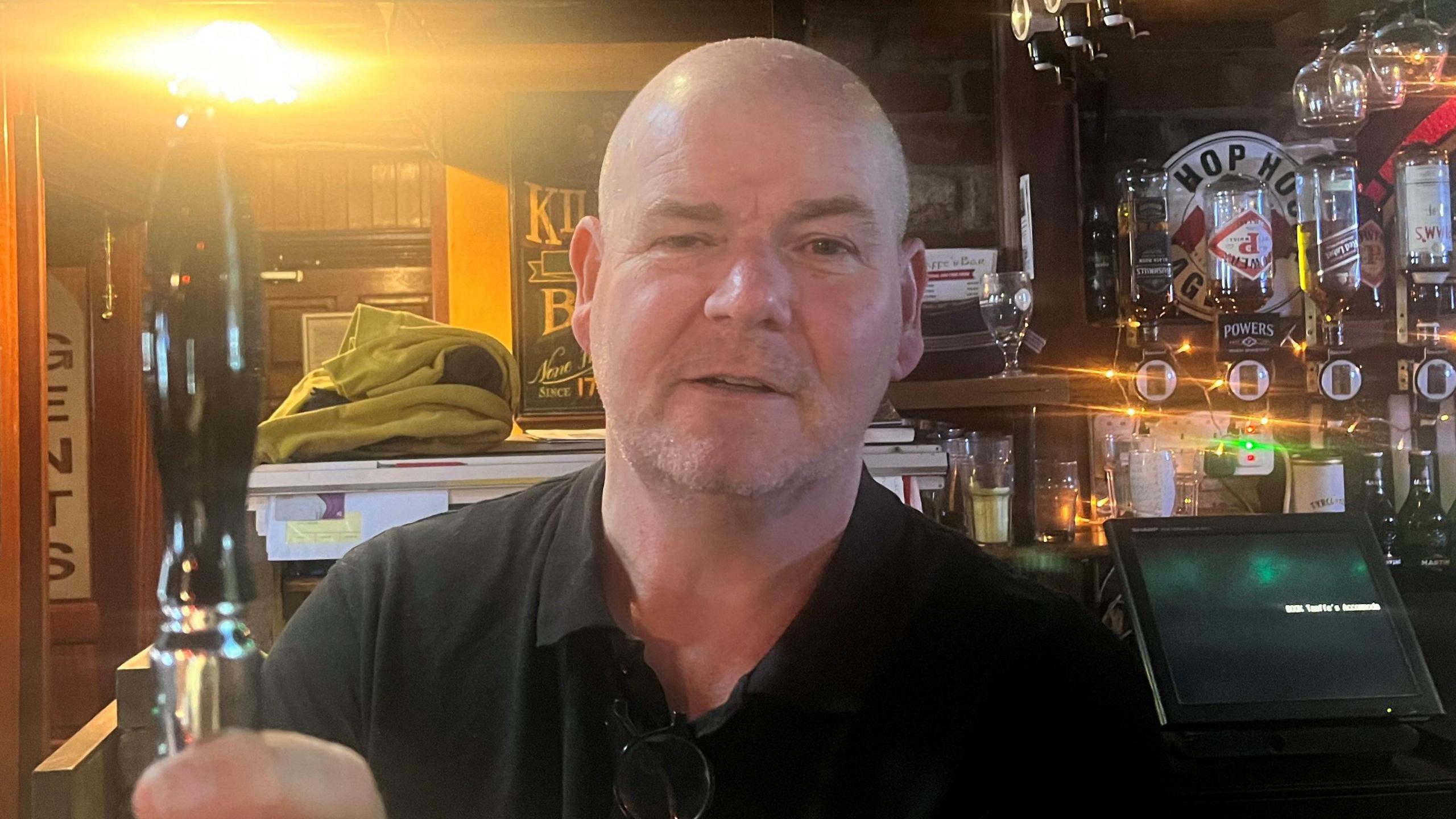 A man in a black polo shirt standing behind a bar