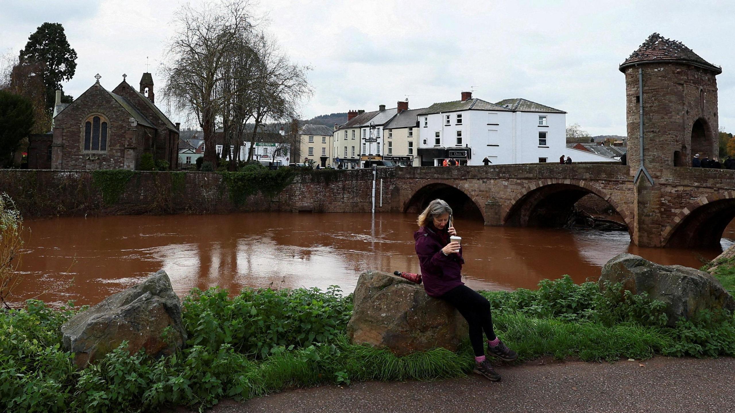 A woman sits near the Monnow river after severe flooding caused by Storm Claudia, in Monmouth,