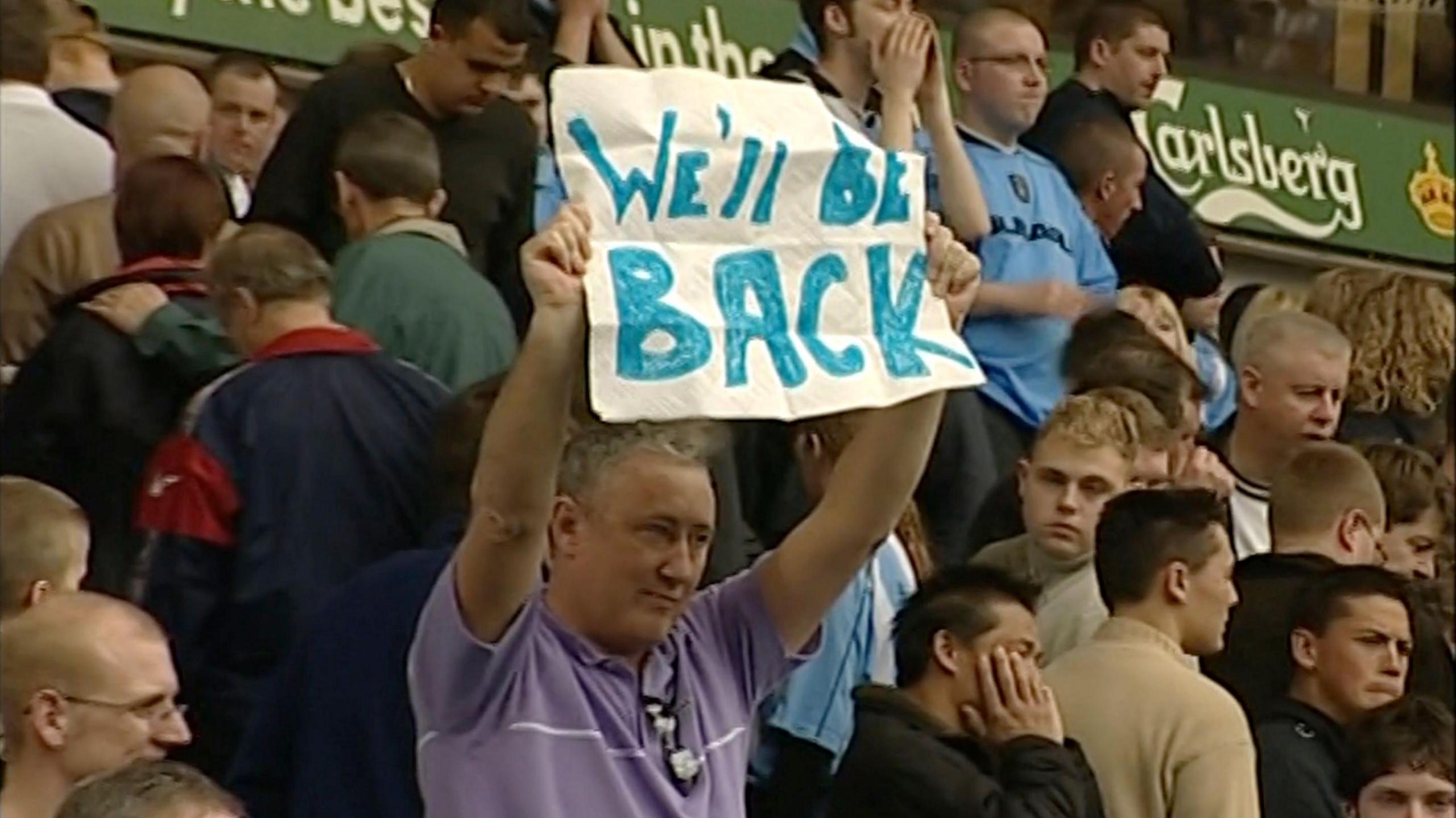 Coventry City fan John Mullaney holds a banner which writes "We'll be back" following the club's relegation from the Premier League.