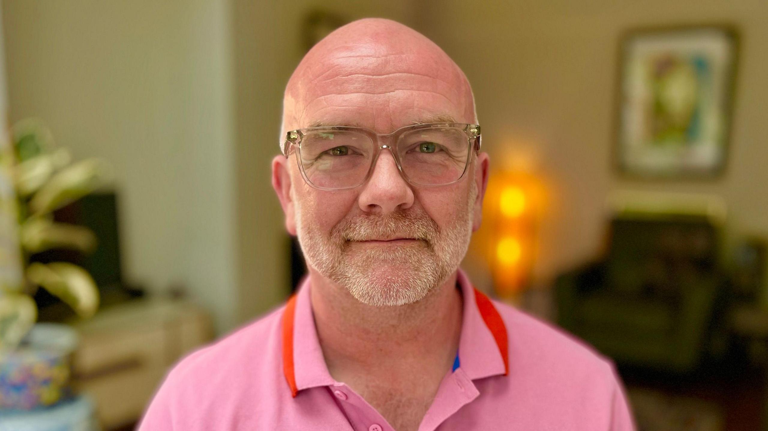 Head and shoulders photo of Clive sitting in a living room, wearing a pink polo shirt 