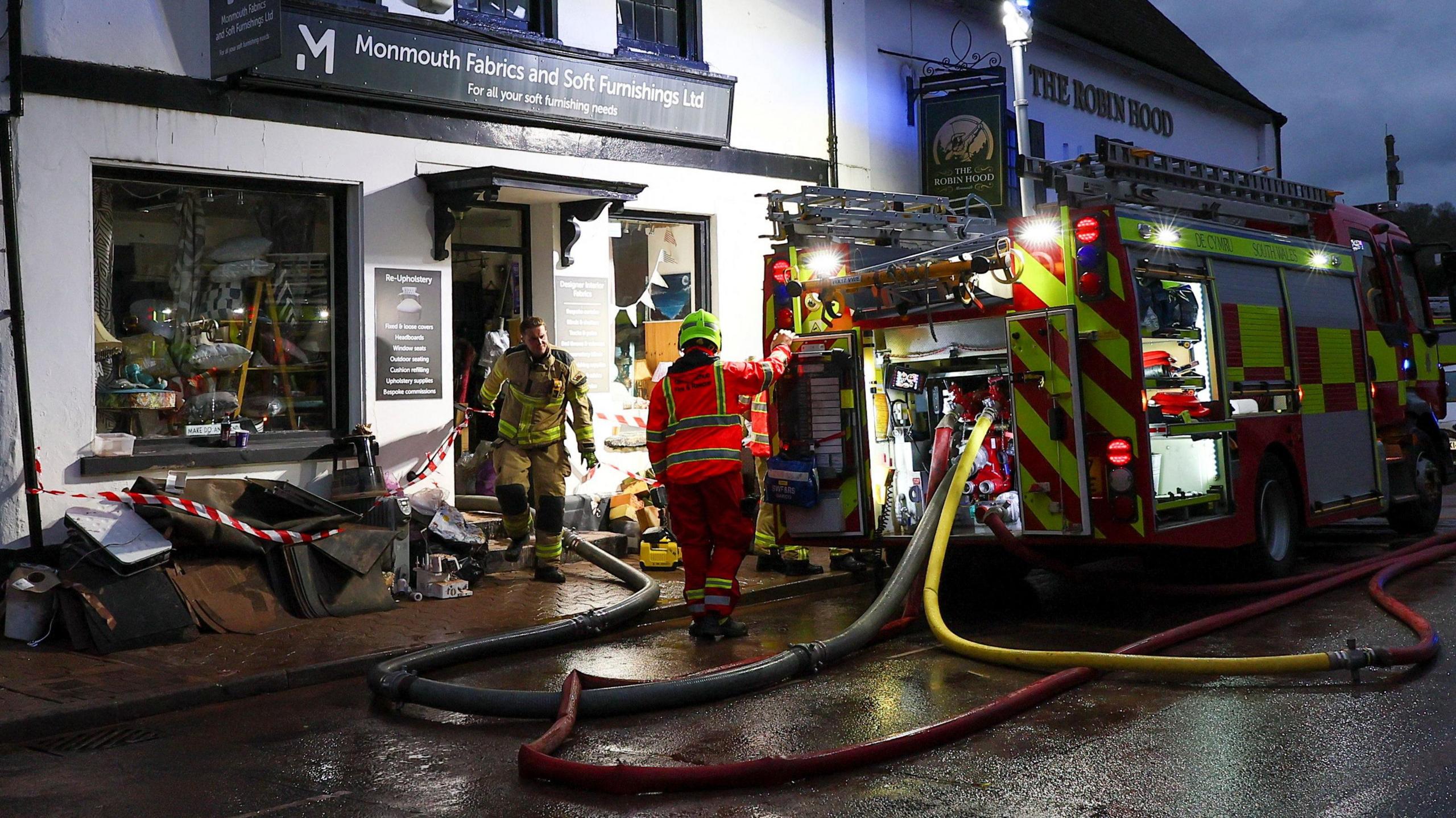 Members of the emergency services work in a shop affected by severe flooding caused by Storm Claudia in Monmouth, Wales