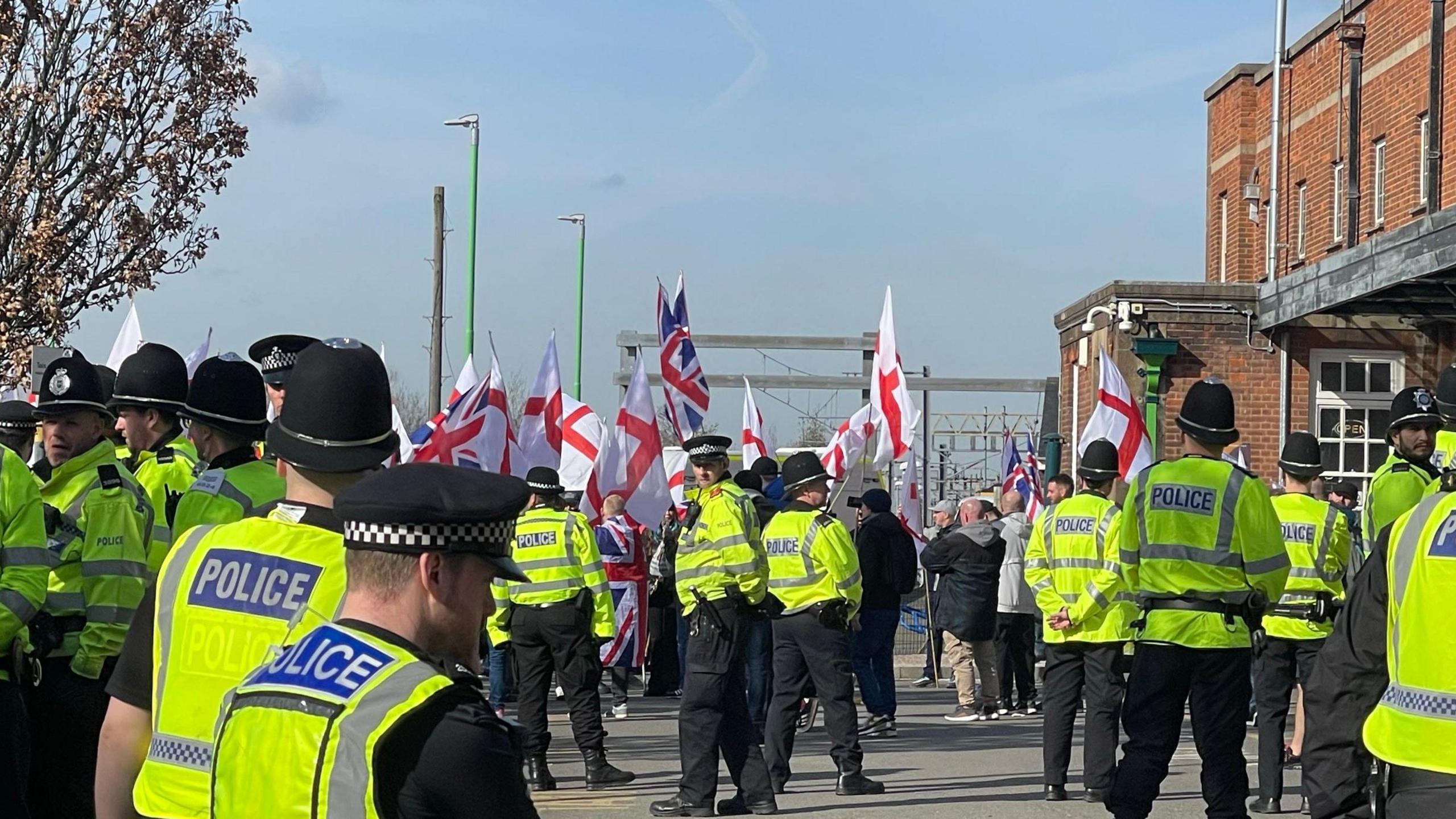 Many police officers with their backs to camera facing a group of protestors holding England flags and Union Jacks