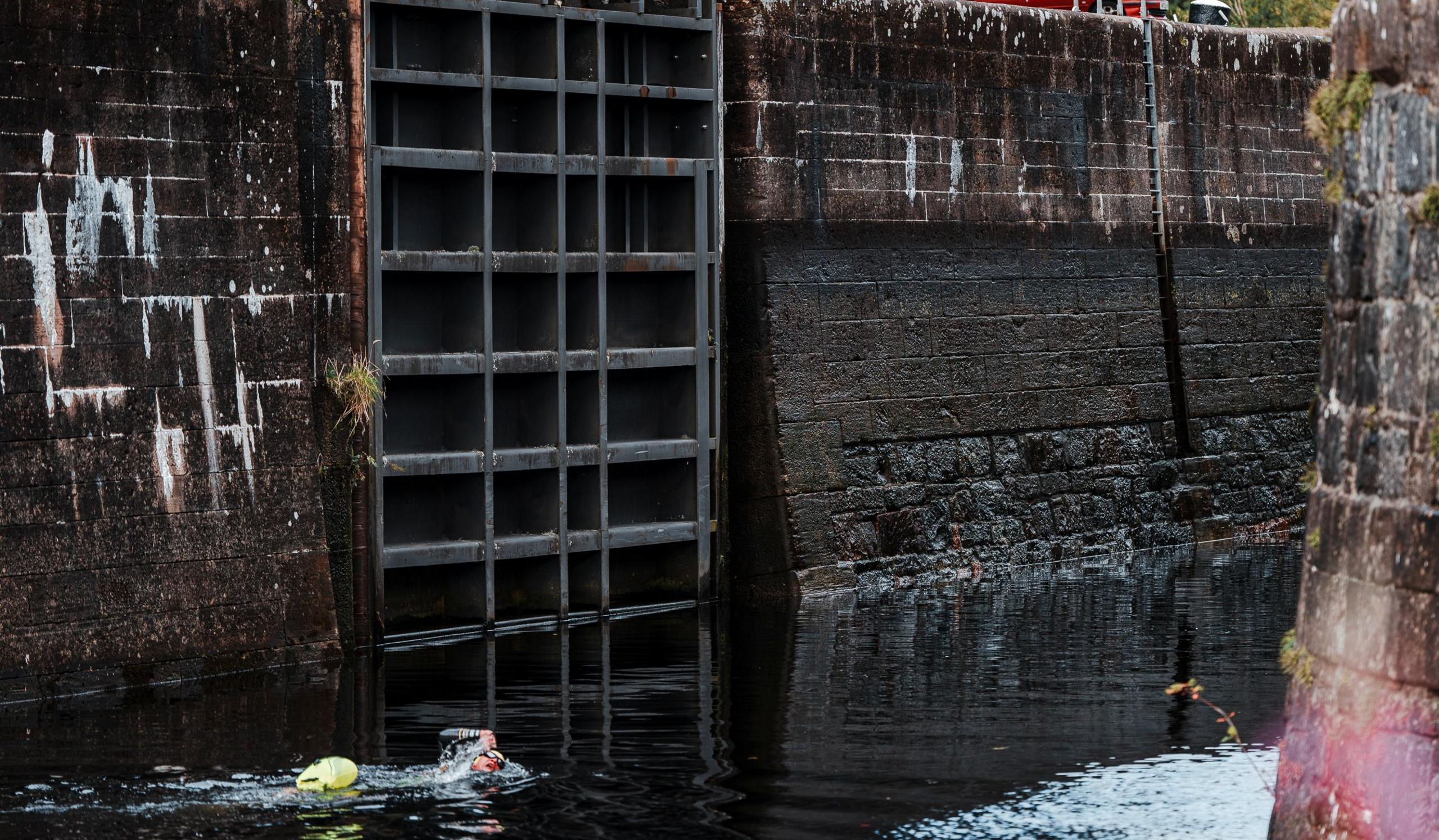 Iain can be seen at the bottom of the picture swimming through still, dark waters of the canal. High, wet brick walls are either side of him.