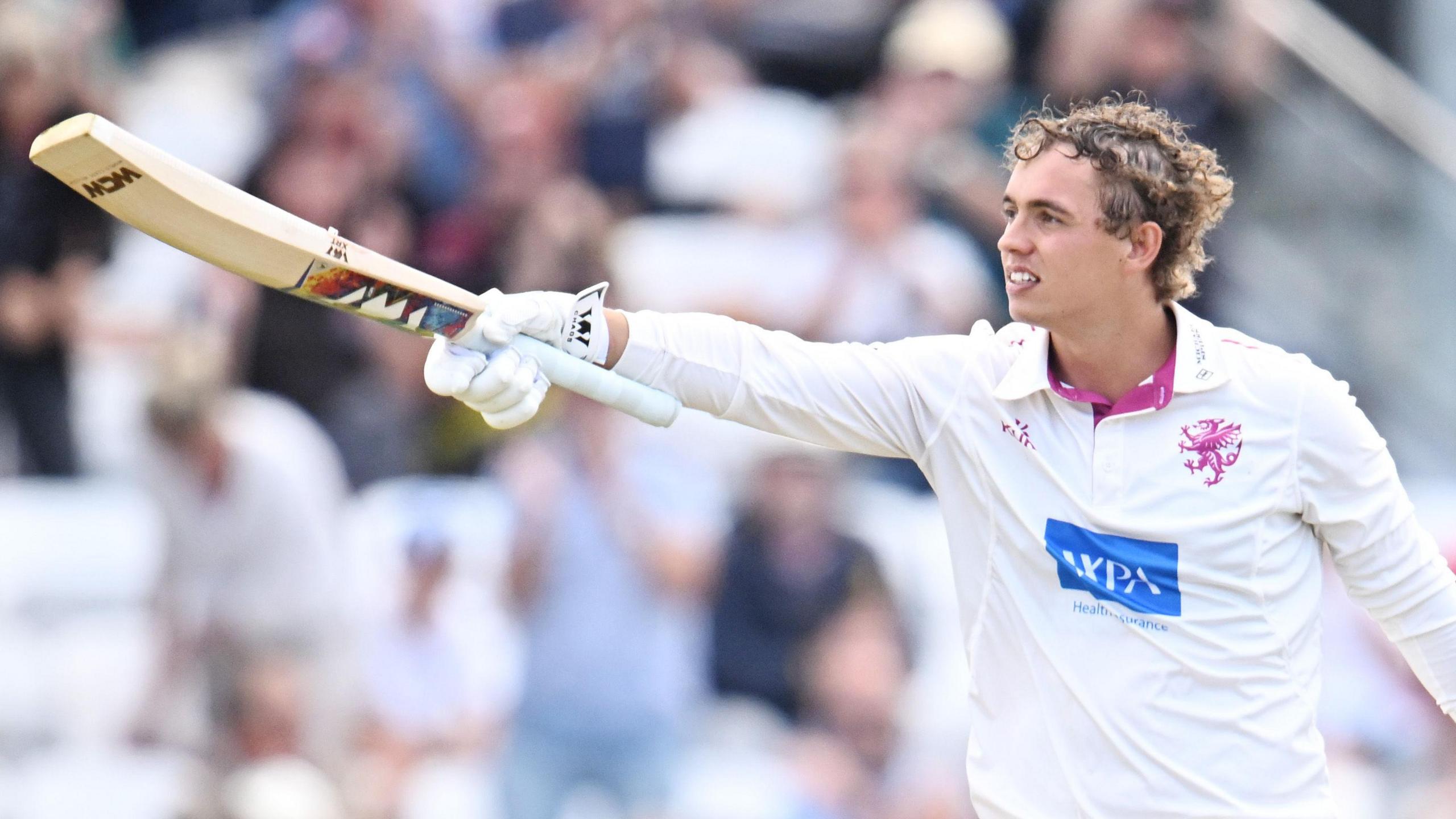 Josh Thomas has his helmet off and points his bat towards the dressing room after scoring a century for Somerset