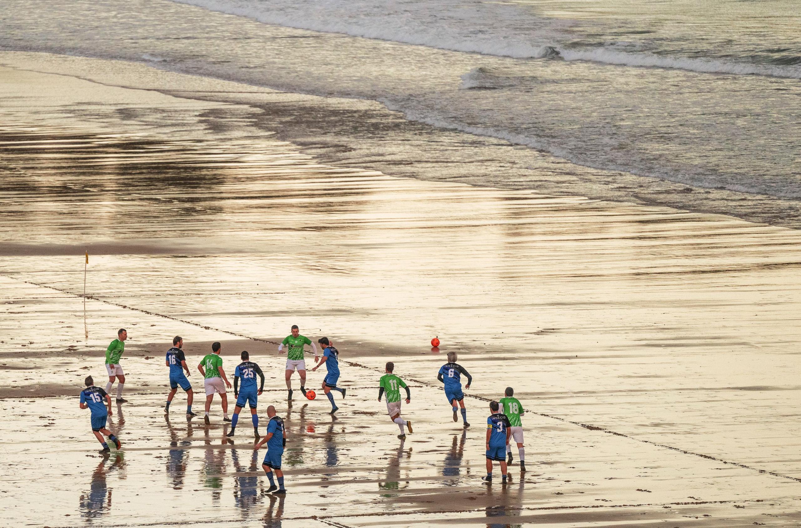 Veteran football players play on the wet sand their beach soccer match of the ninth matchday of the 64th Campeonato de Futbol Playero de Santander at the Sardinero Beach