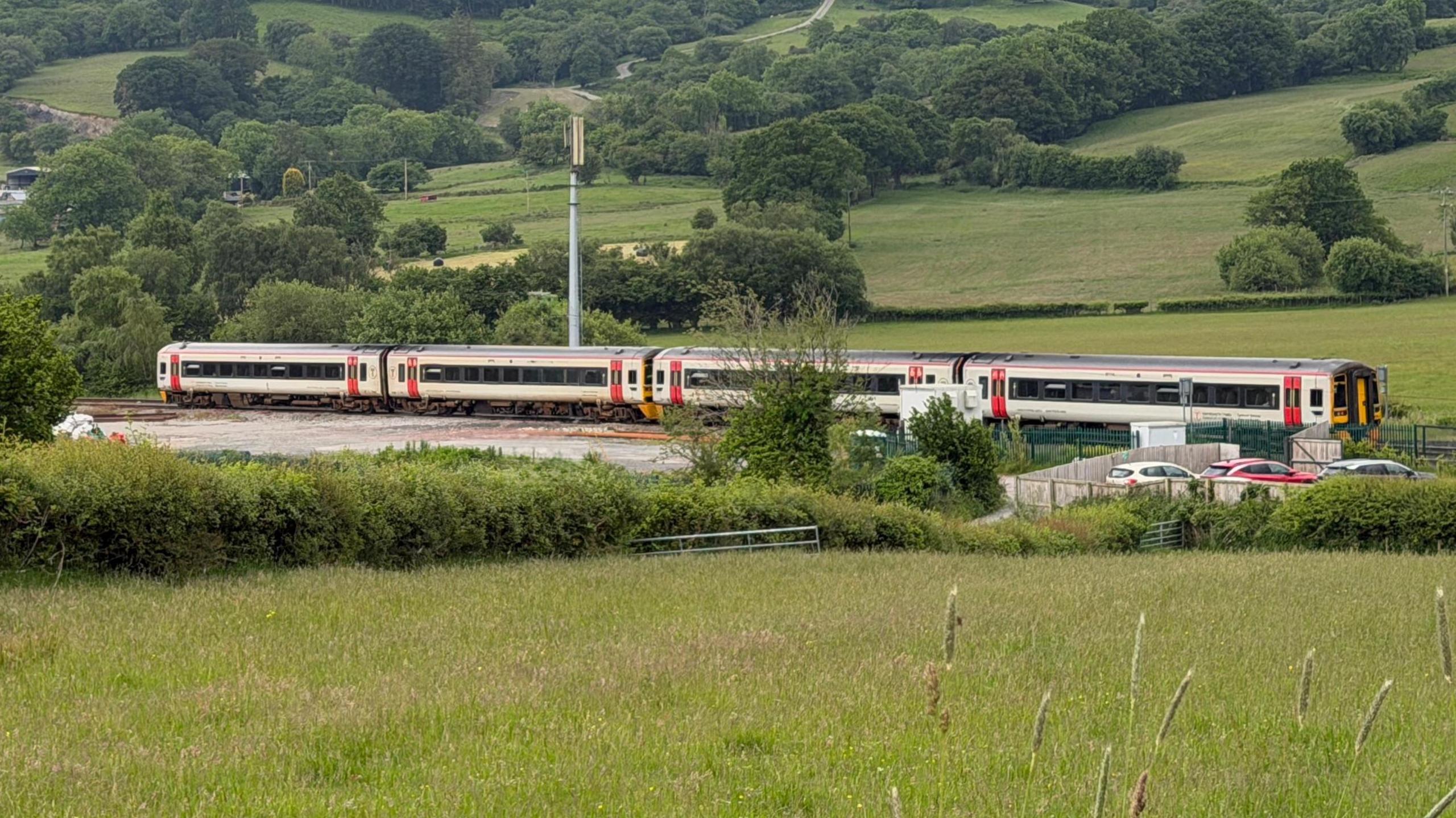 Tren gyda pedwar cerbyd yn llonydd ar y cledru tra'n aros i'r tren arall ei basio. 