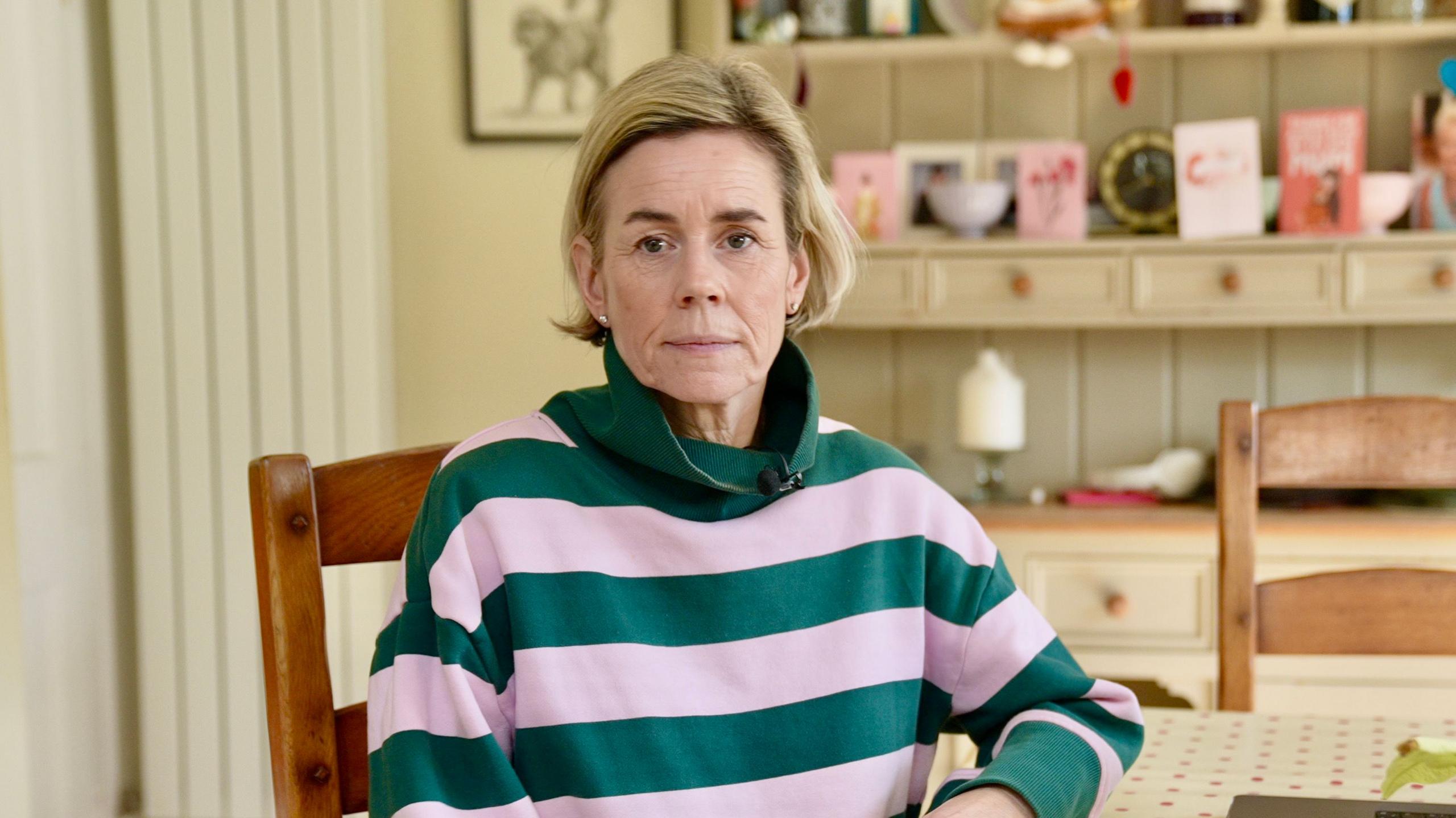 Kate Speirs, e ulur në një dhomë, duke parë drejt e në kamerë, e veshur me një bluzë rozë dhe jeshile, ajo ka flokë të shkurtër bjonde dhe vathë në të dy veshët. Ajo e ka dorën mbi një tavolinë dhe është ulur në një karrige pishe. Pas saj është një komodinë me kartolina dhe zbukurime sipër.