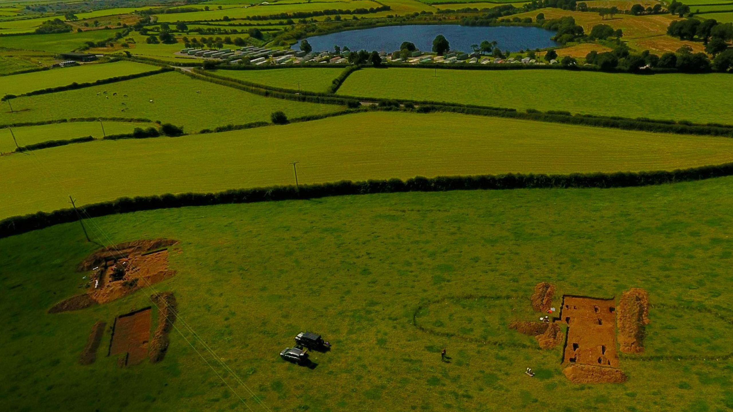 An aerial view of the excavation sites. Two sections of a green fields have been dug up, revealing the soil underneath.