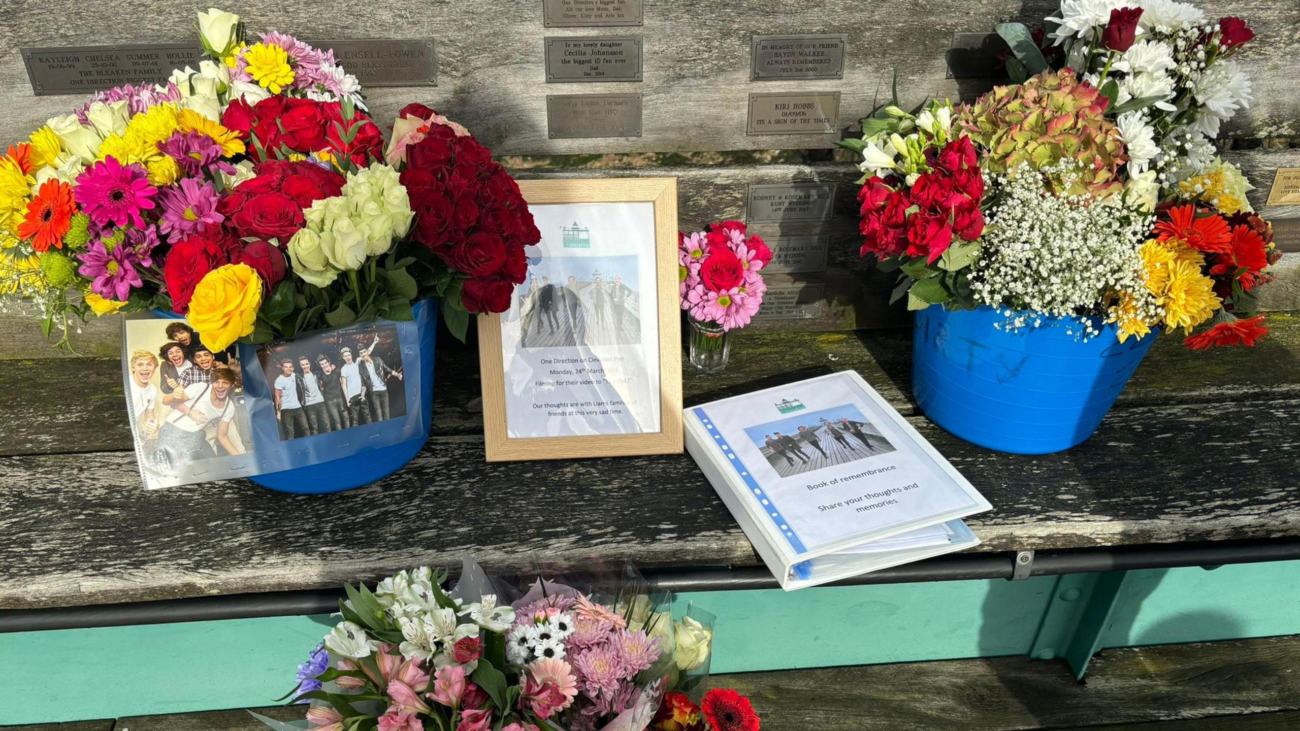 Floral tributes left at Clevedon pier in memory of Liam Payne. There is also a printed image of the boyband and a file for fans to leave their written condolences. 