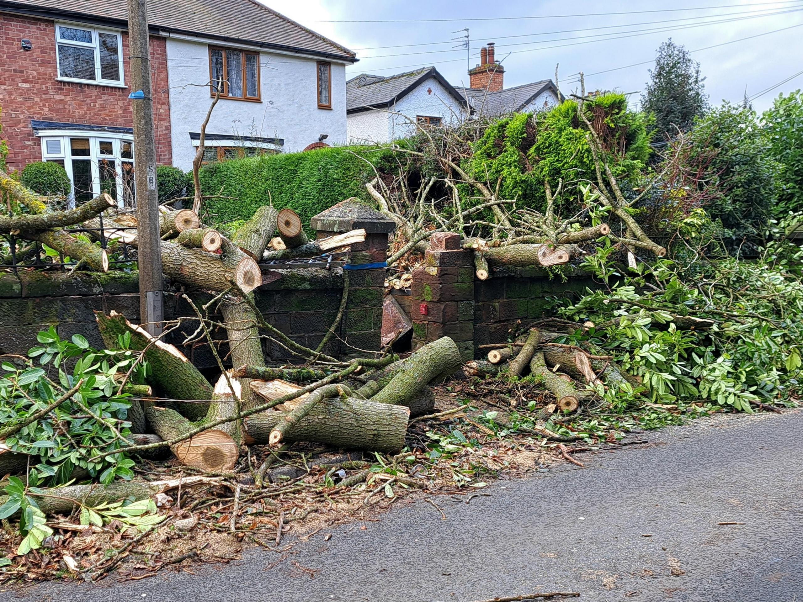 Sawn tree branches and other debris beside a road in Codsall, with homes in the background