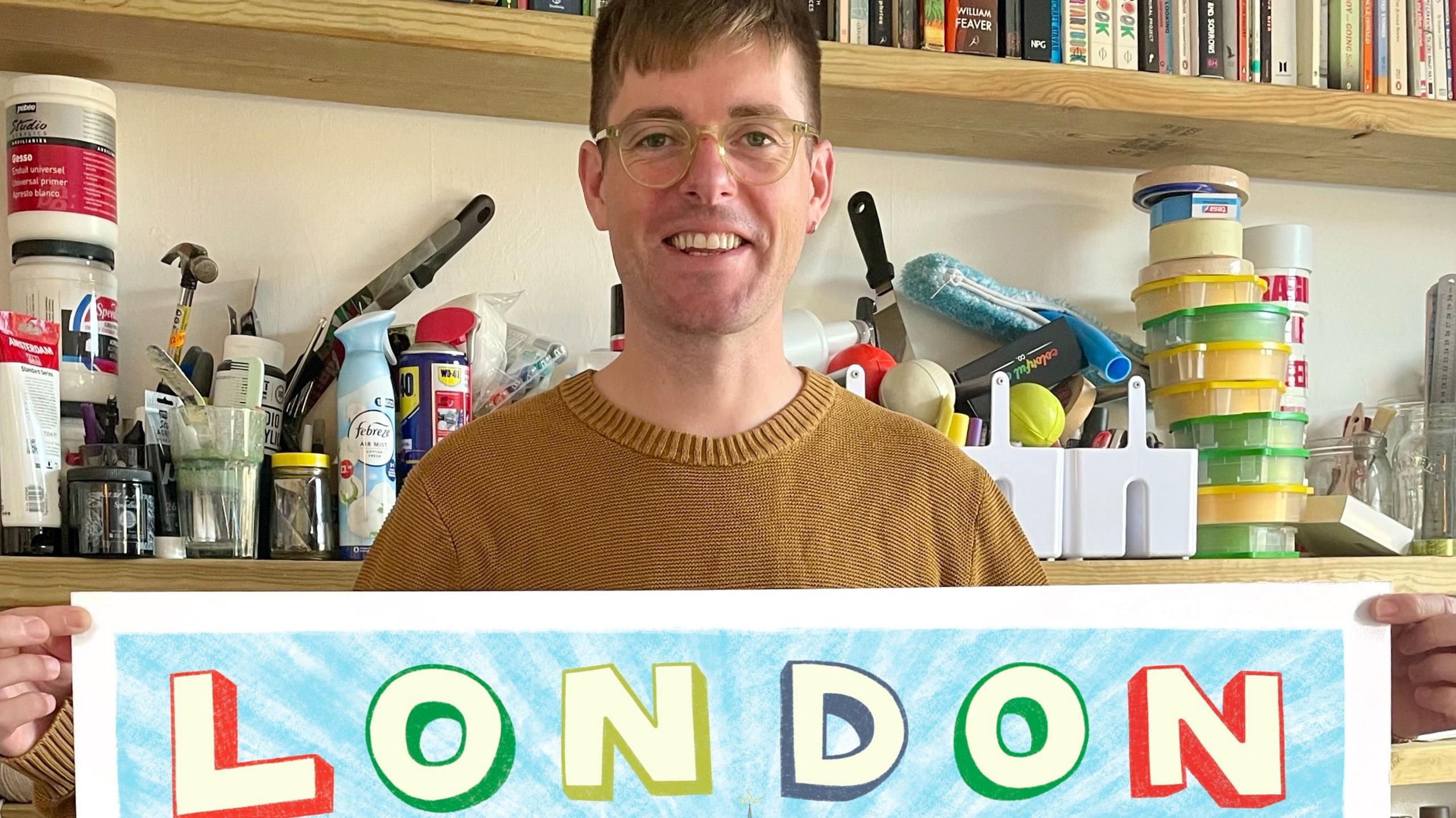 Angry Dan holding a copy of his map with London written on the top and shelves behind him