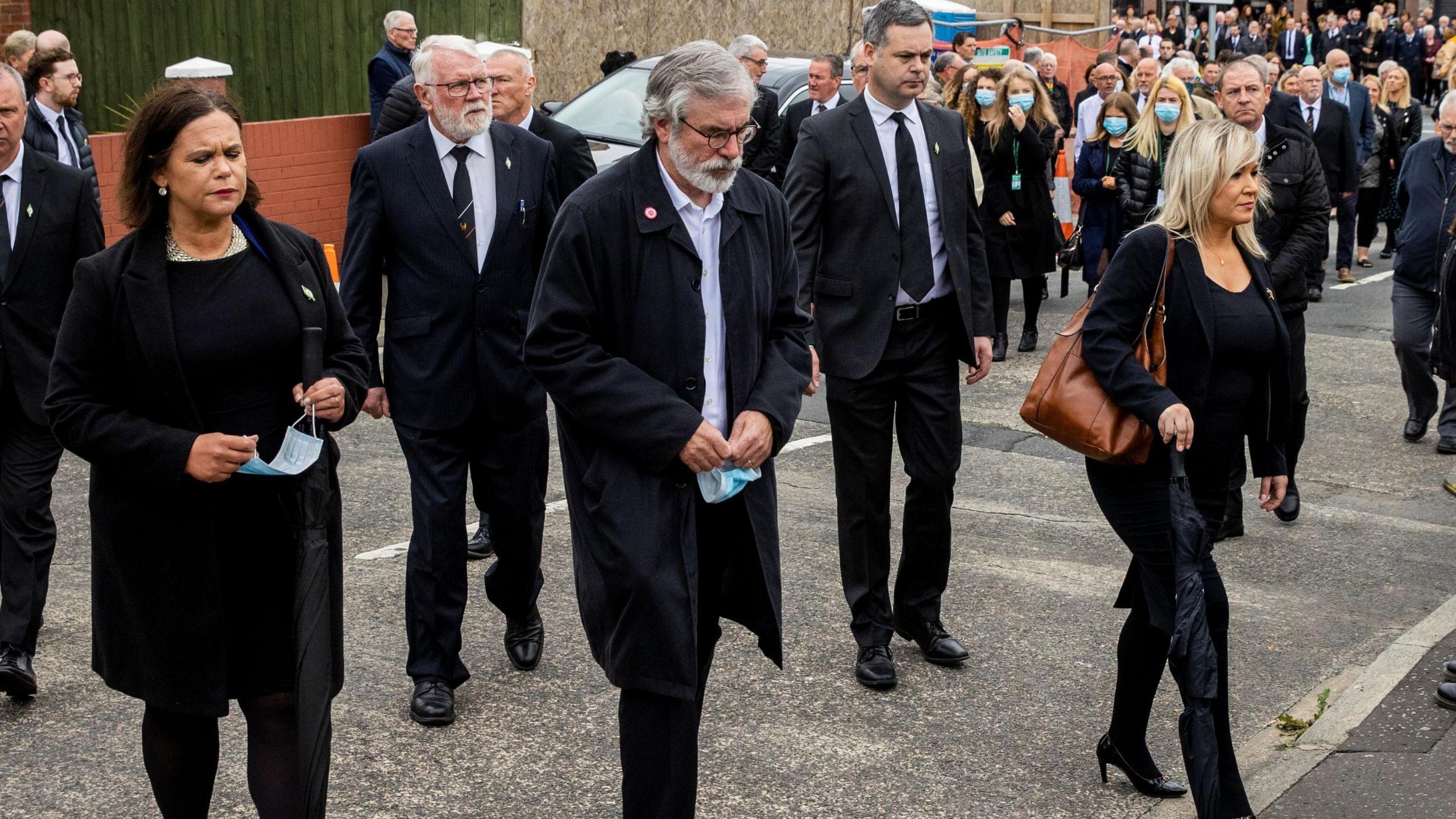 A group of people walking they are all dressed in black.