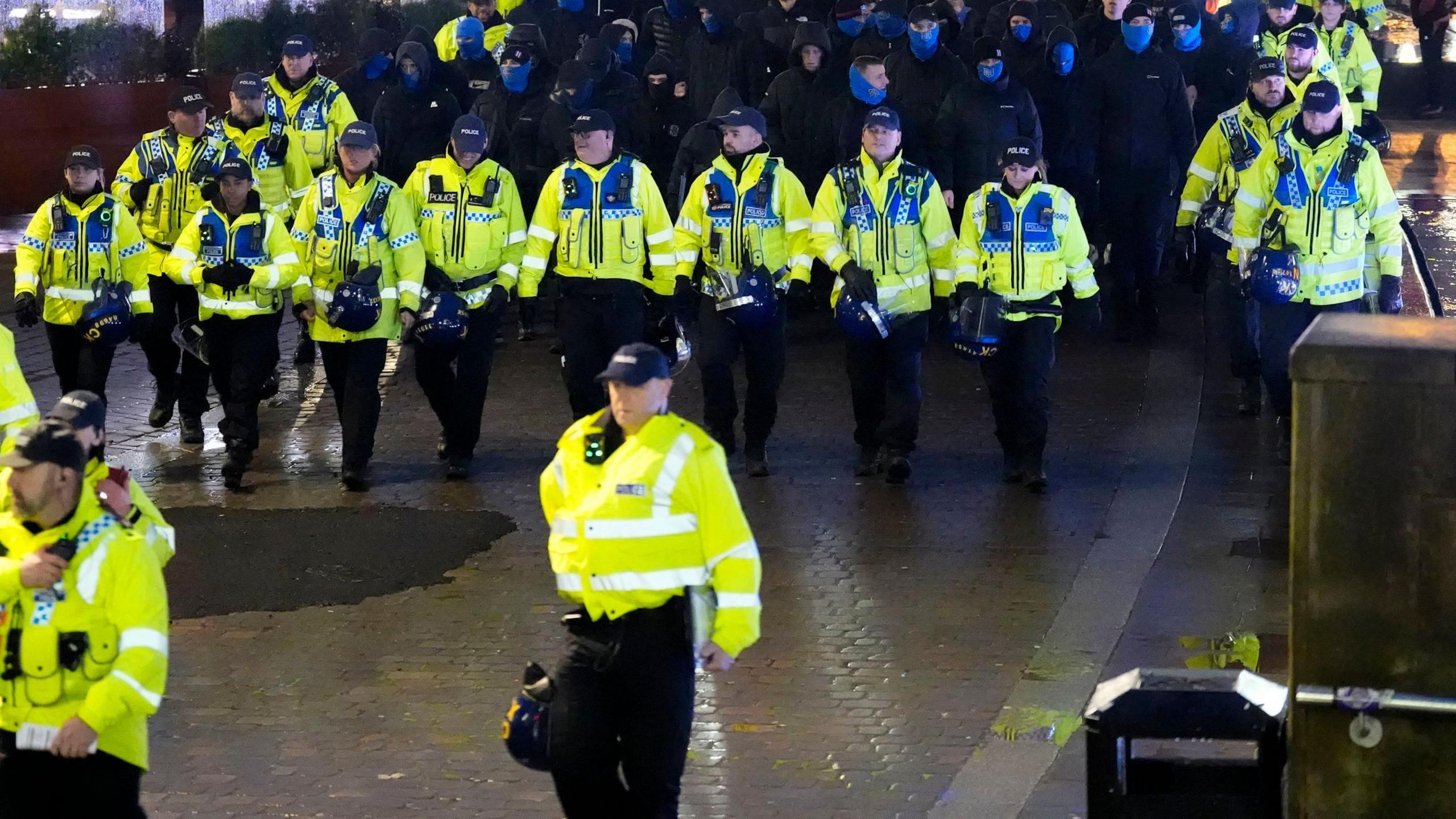 A line of police in yellow high-vis walk in front of Rangers fans in Manchester, ahead of their team's UEFA Europa League League Stage fixture against Manchester United.