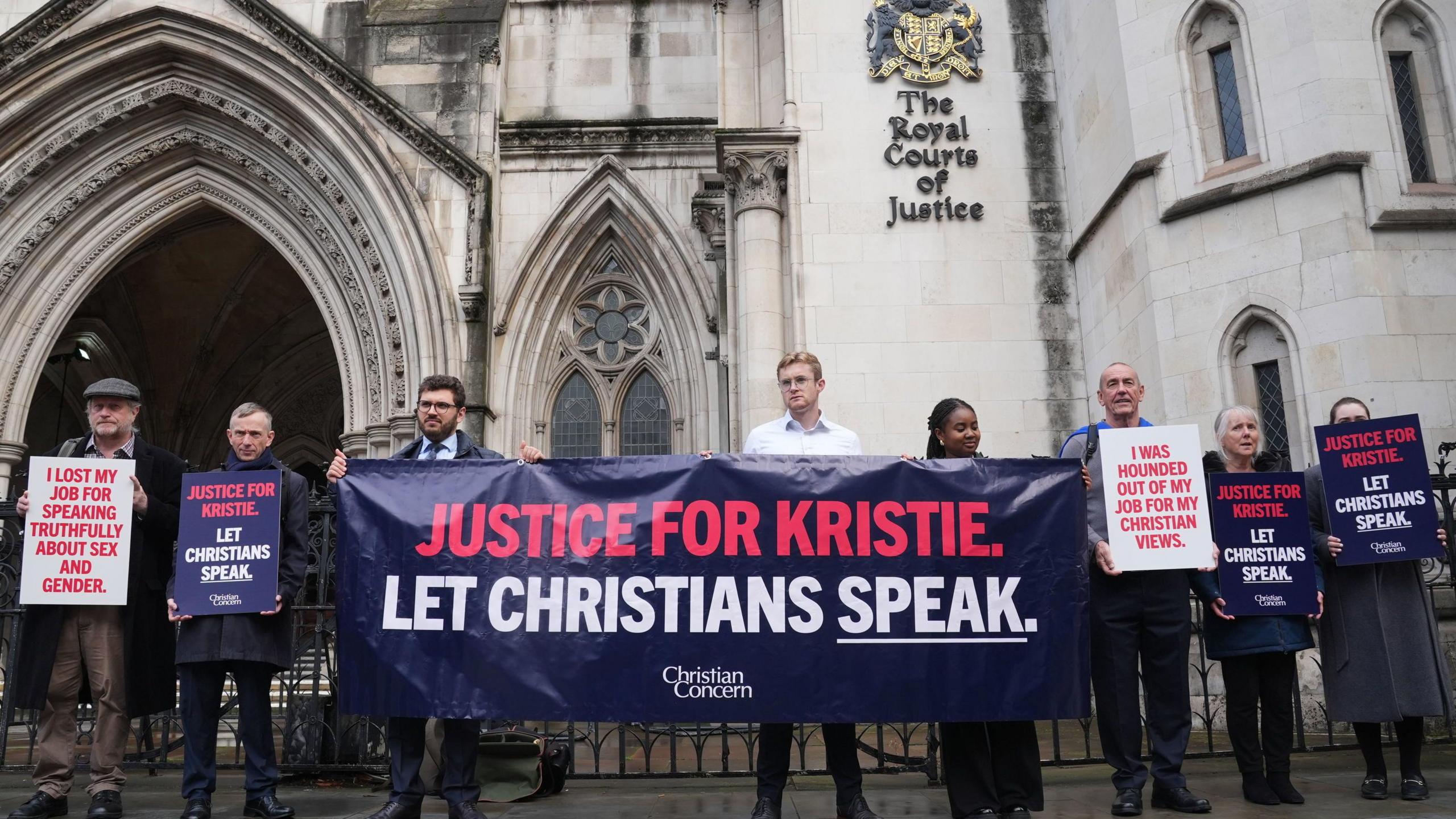 A crowd or people outside the Royal Courts of Justice hold a banner reading "Justice for Kristie. Let Christians Speak."