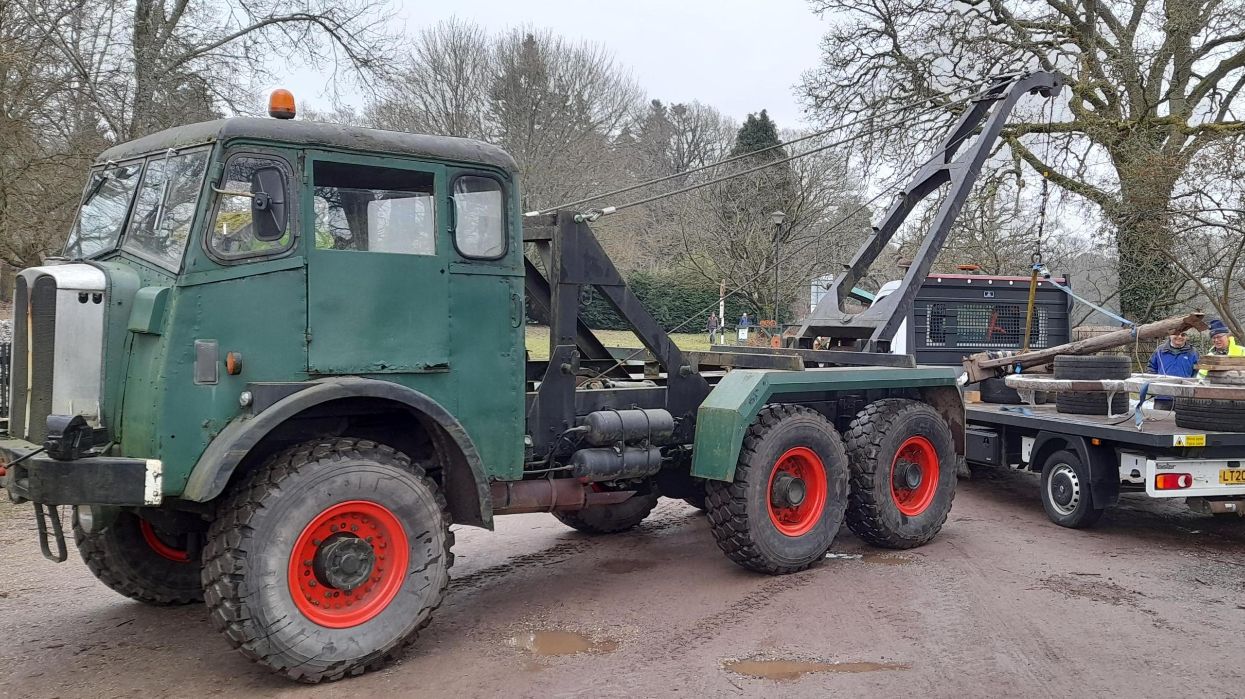 A green timber crane, which looks like a large truck, lifts part of the carriage into the air.