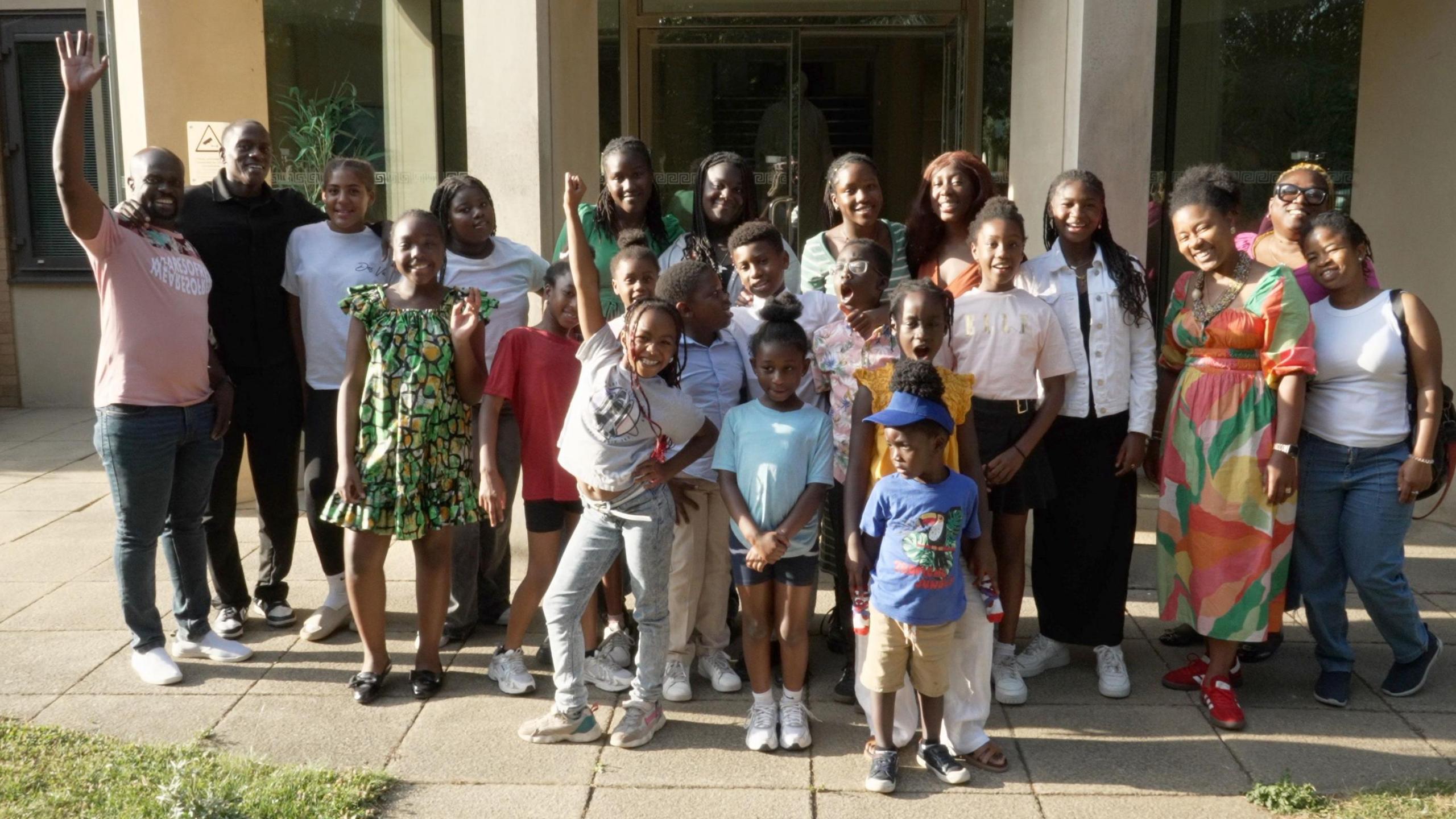 A group of about 20 black children and their parents pose for a photograph outside Wolfson College in Cambridge.