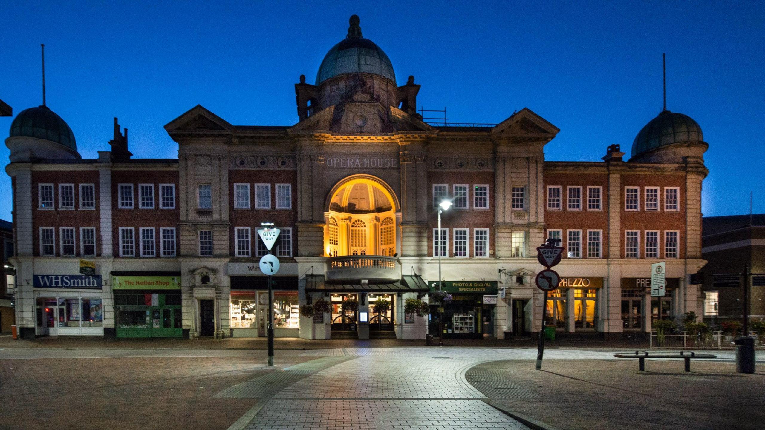 A view from the street of the Opera House in the evening. It is a large, regal building with "Opera House" written in white letters on the front.