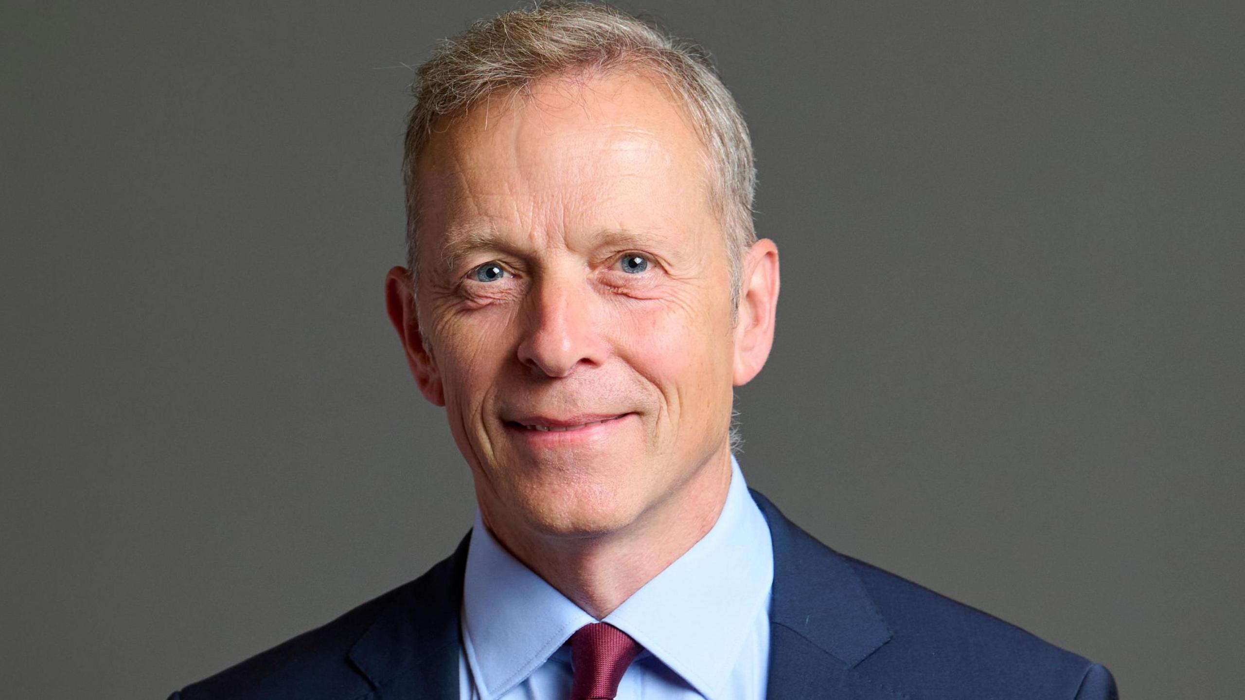 An official portrait of Matt Rodda, who is wearing a dark blue jacket, light blue shirt and maroon tie 