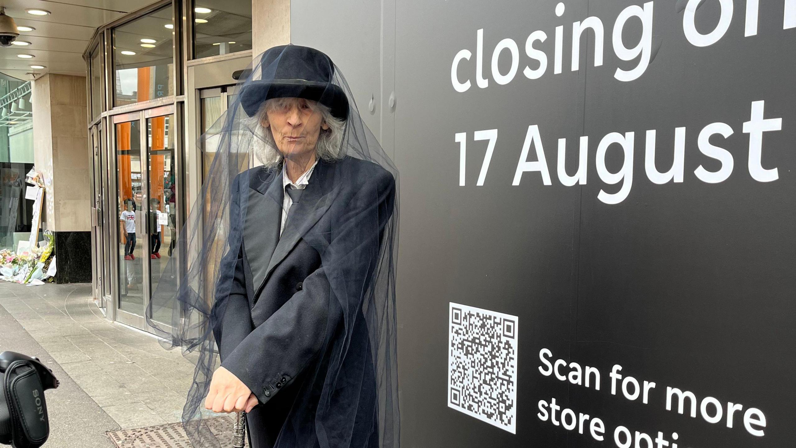 A woman dressed in black with a veil to mourn the closure of a shop