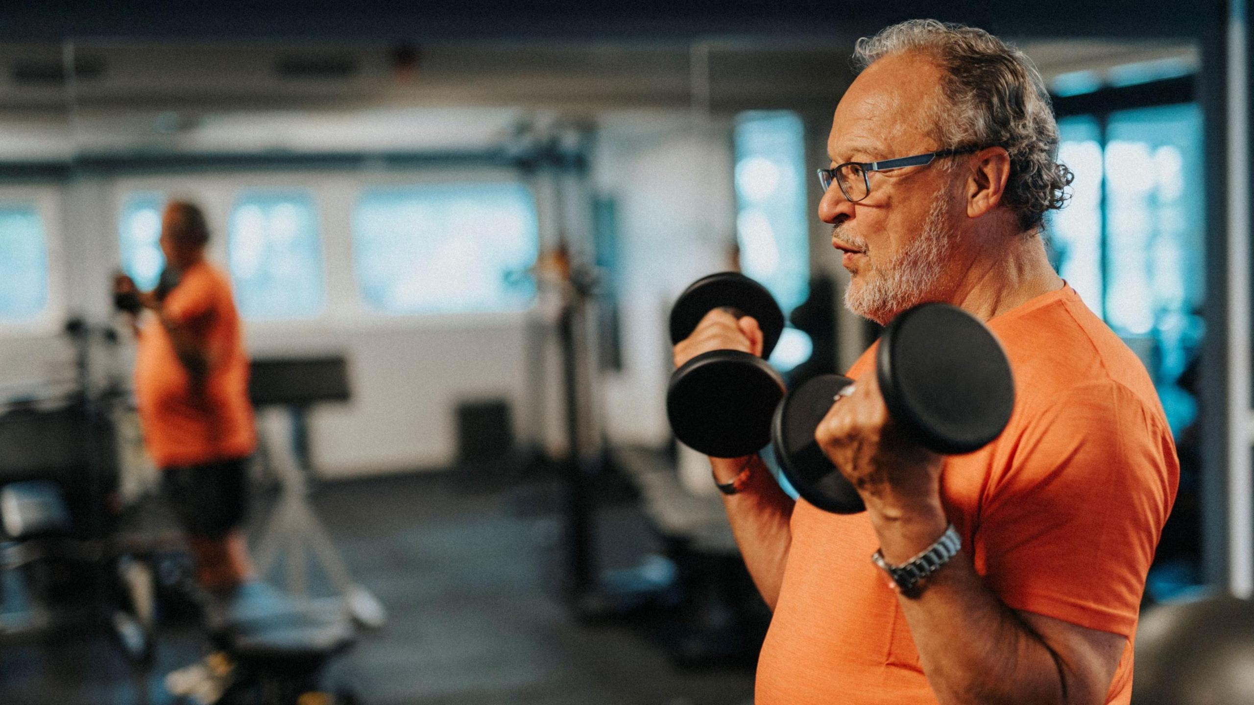 A man earing an orange T-shirt holding weights at the gym