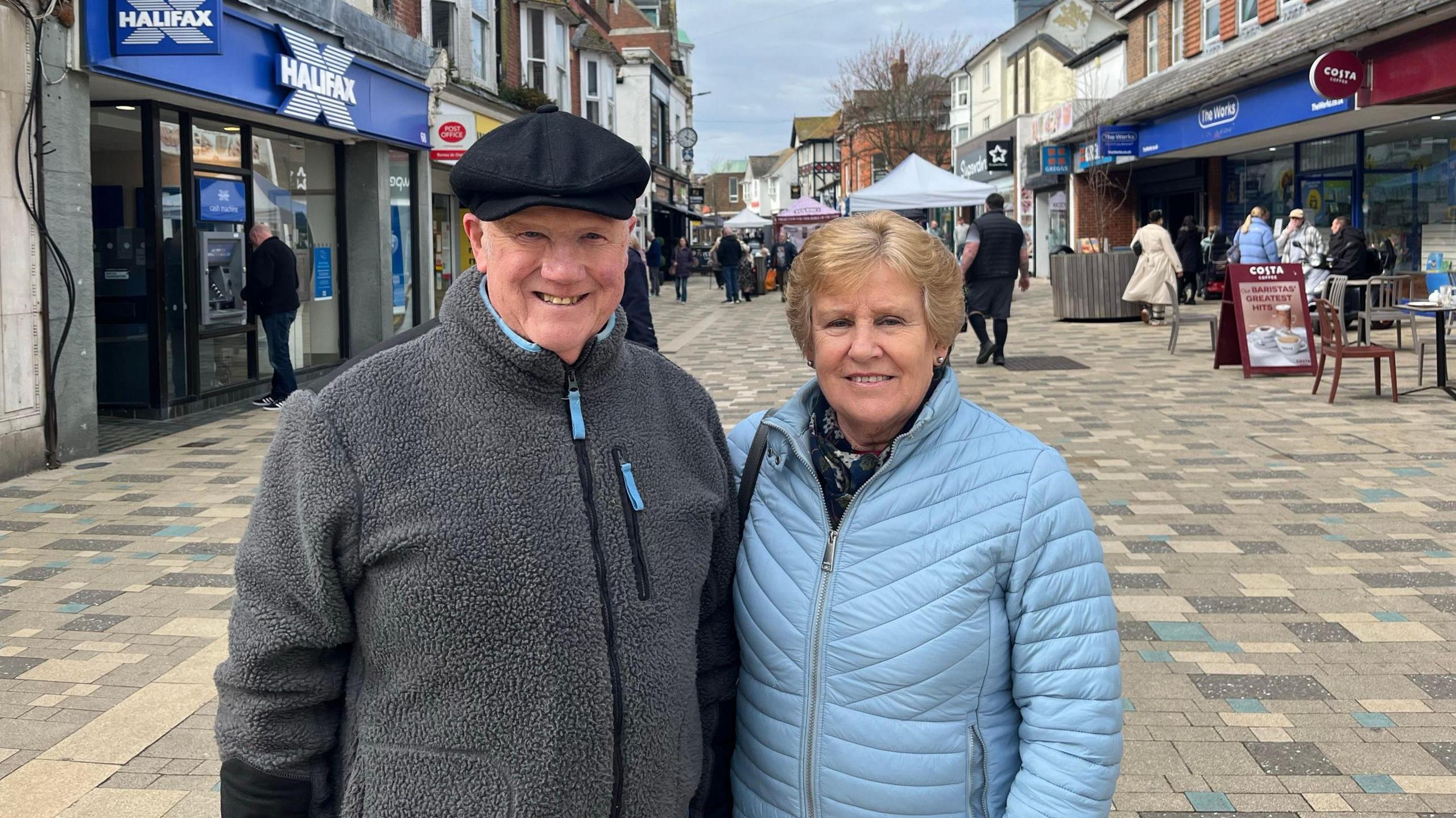 A man in a grey fleece wearing and a black hat, and a woman wearing a light blue puffer jacket.