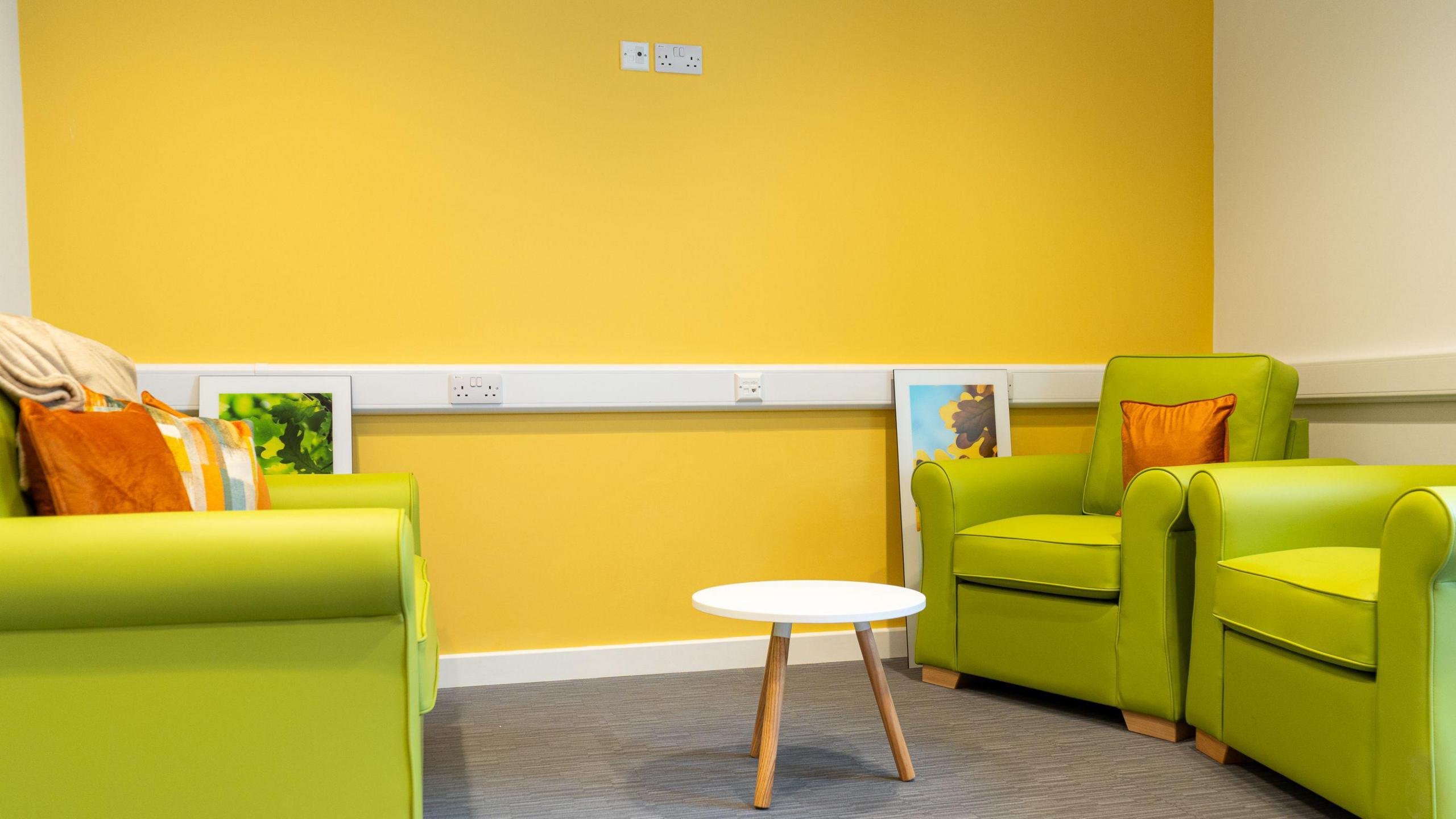 A room with a brigh yellow wall, there are lime green leather chairs and a sofa and a small coffee table in the middle.