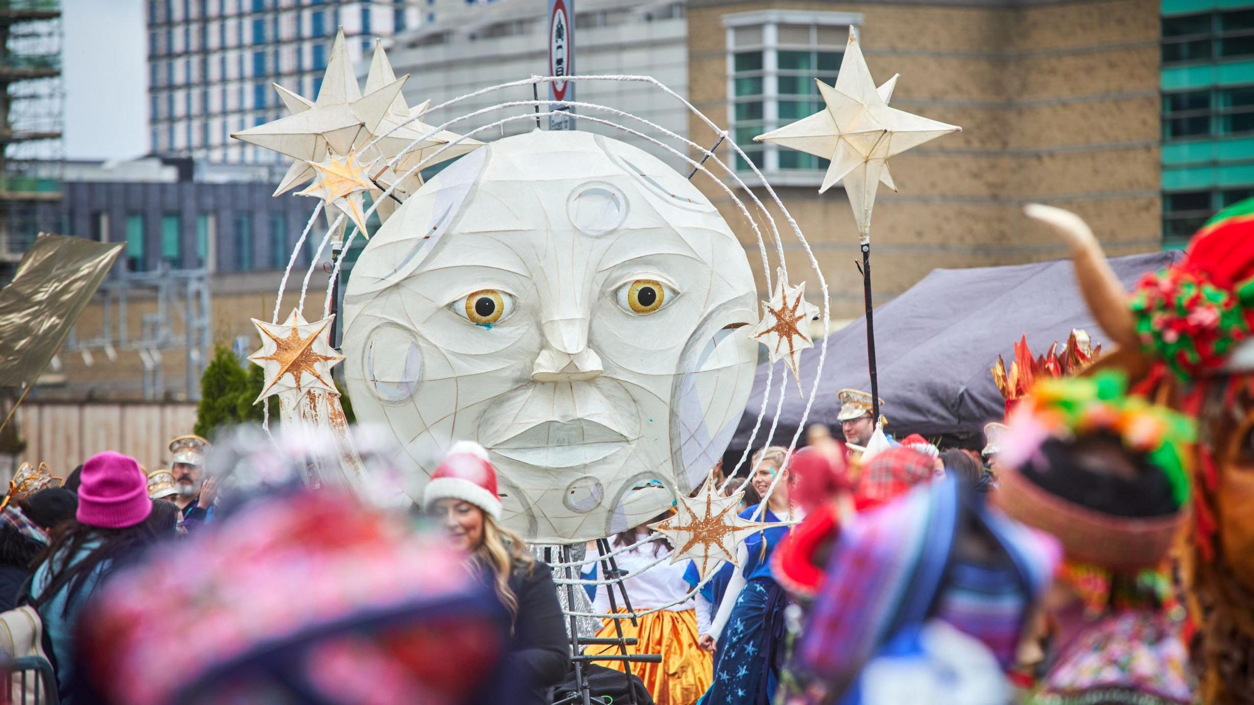 A large artwork of a full moon with facial features looking down over the crowds and surrounded by stars above it