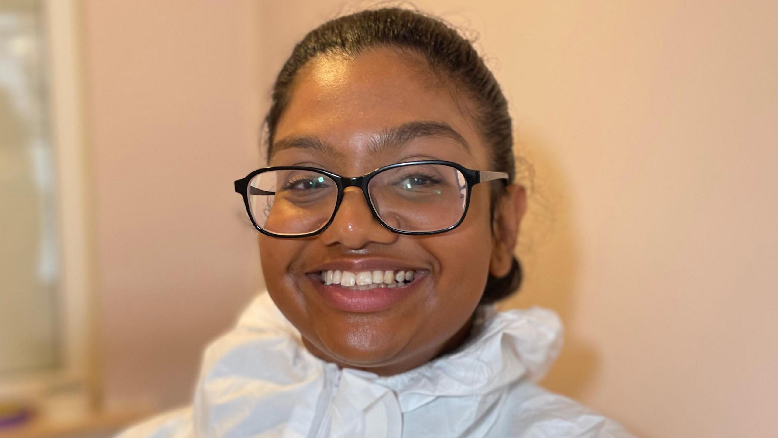 Daveena is wearing a white overall and smiling