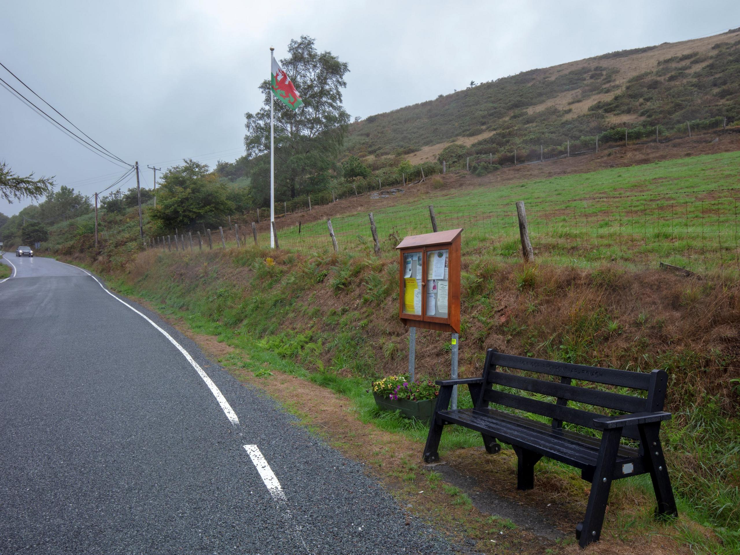 A communal bench next to a notice board on a rural road