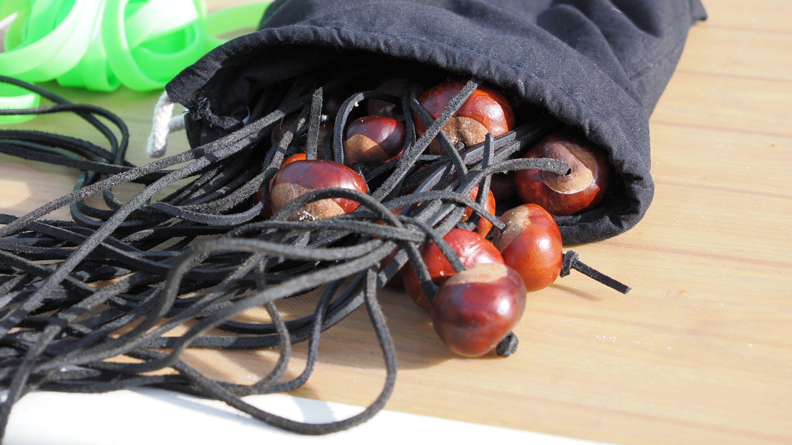 A bag of conkers, with leather straps, in a bag, sat on a table.