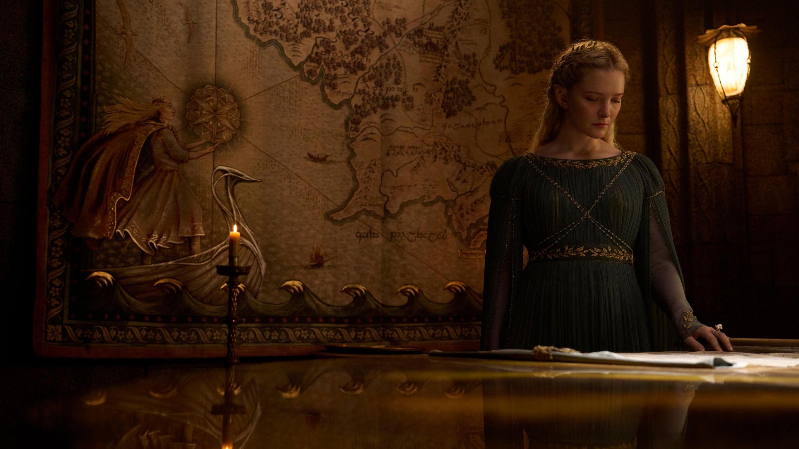 A female elf stands before a map of Middle-earth.