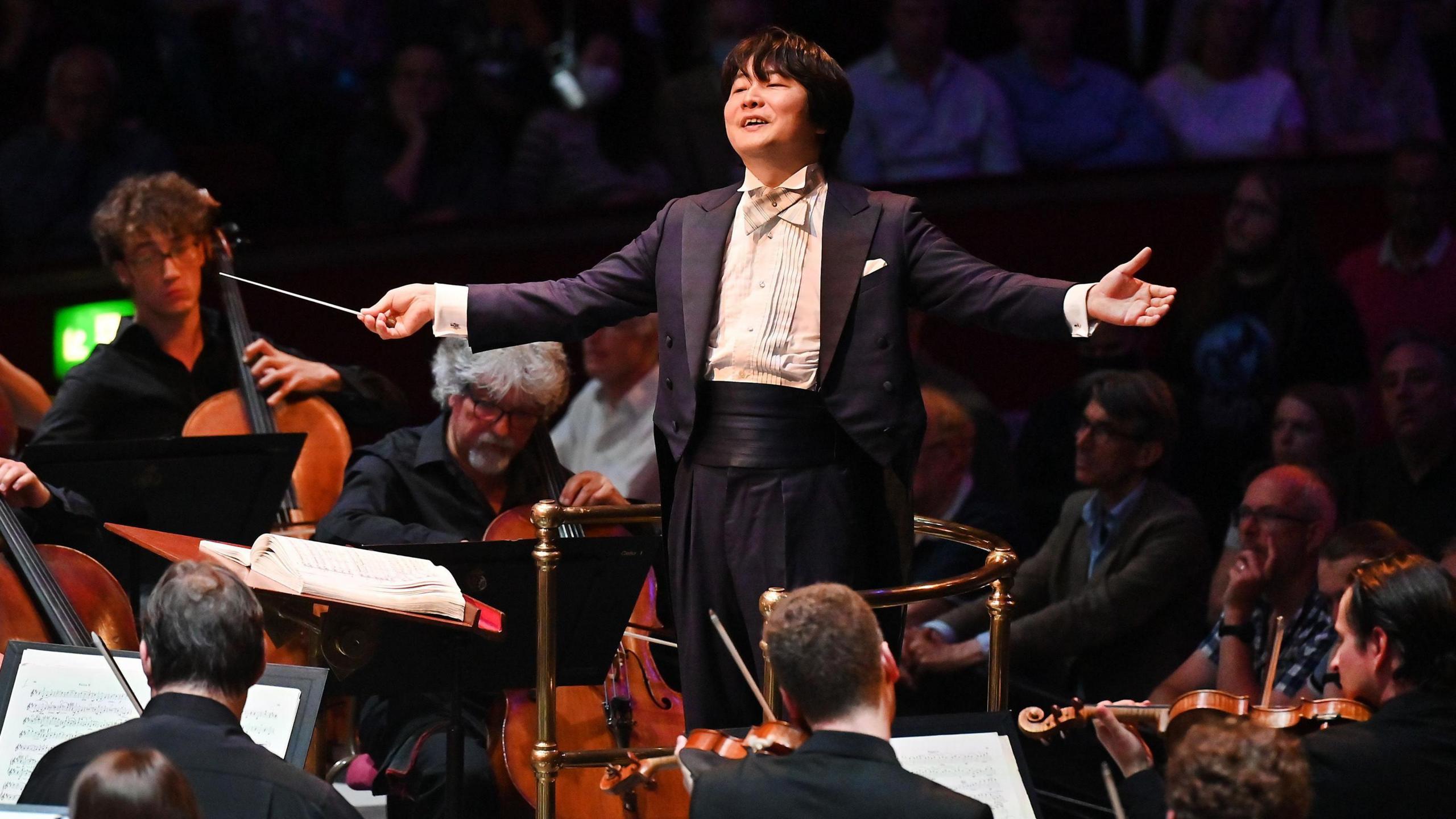 A man conducting an orchestra as the audience watches on