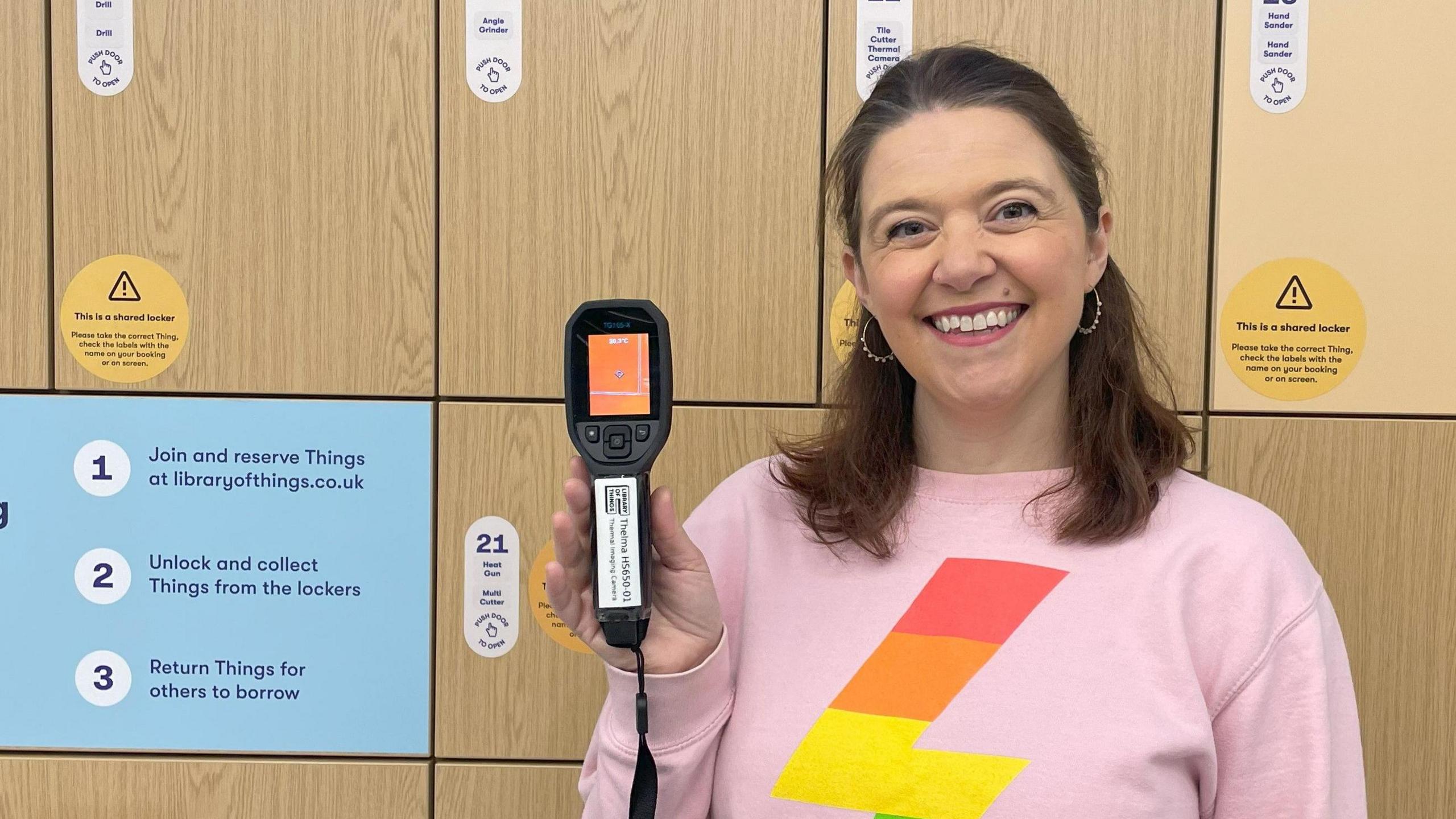 Heather Mullin in a pink jumper holds up a thermal camera