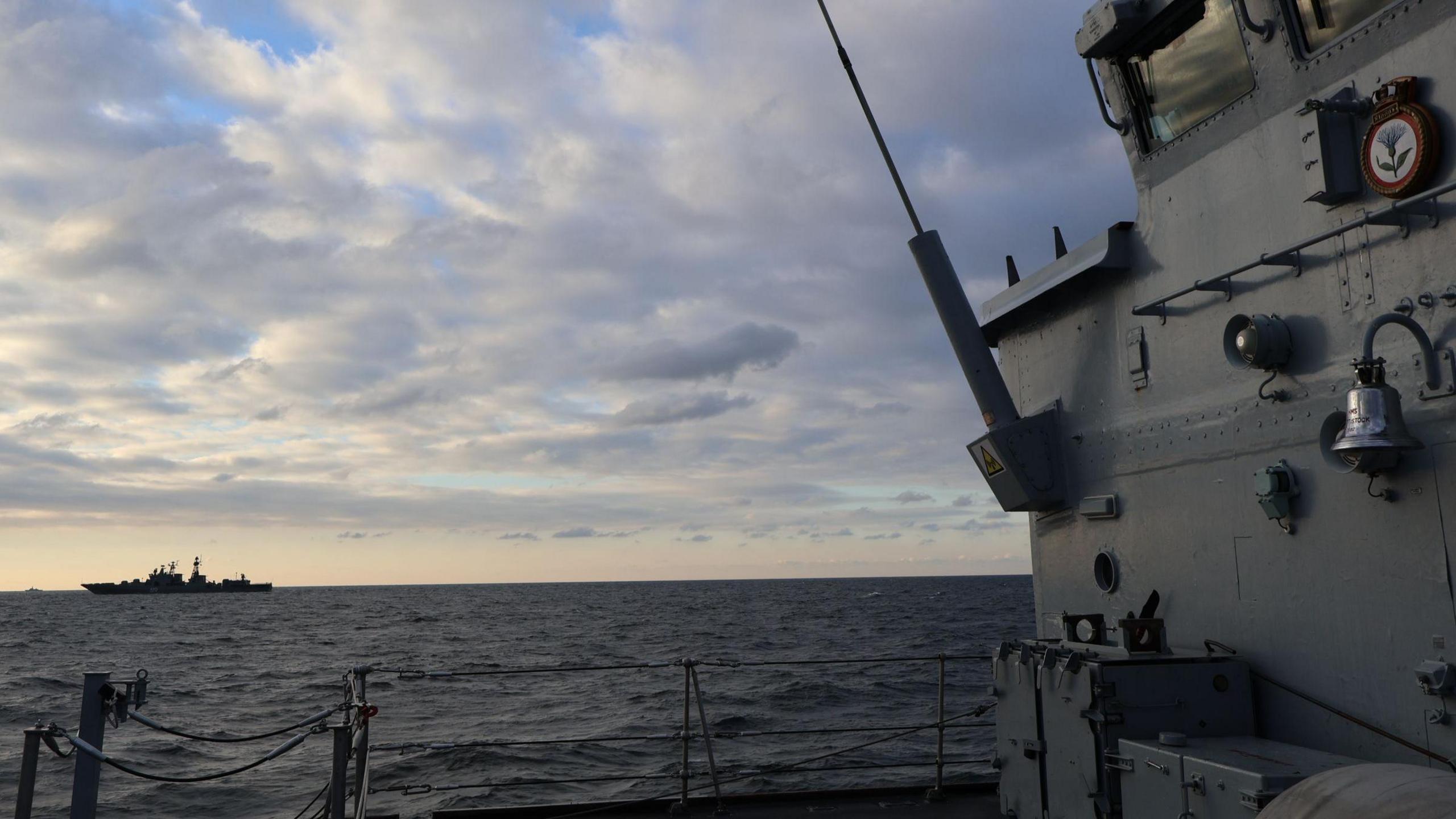 Image is taken onboard HMS Cattistock looking out to sea. On the far left, set against the sunset, the silhouette of RFN Severomorsk 619 can be seen