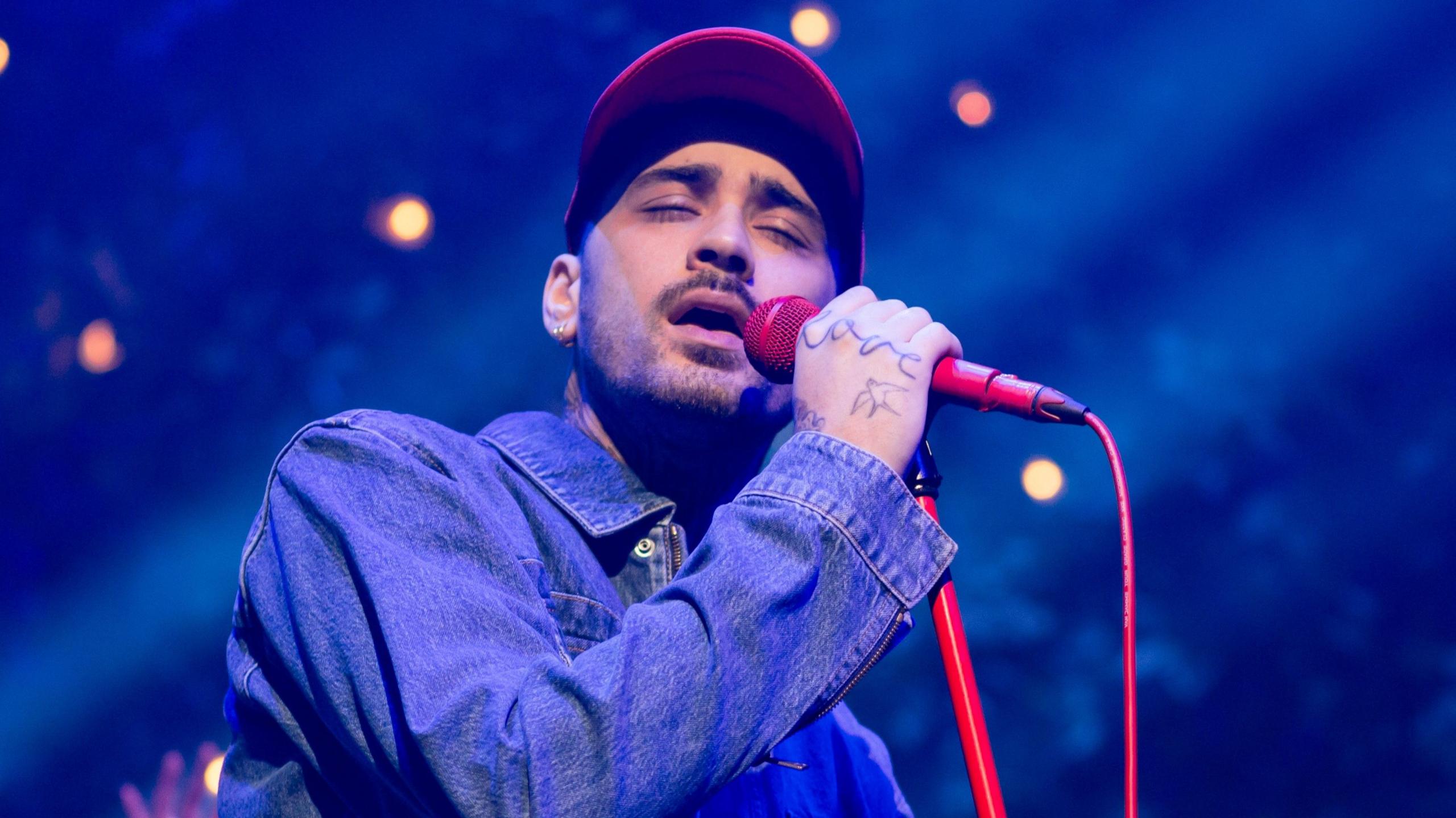 Zayn Malik singing into a red microphone while performing at O2 Academy Leeds 