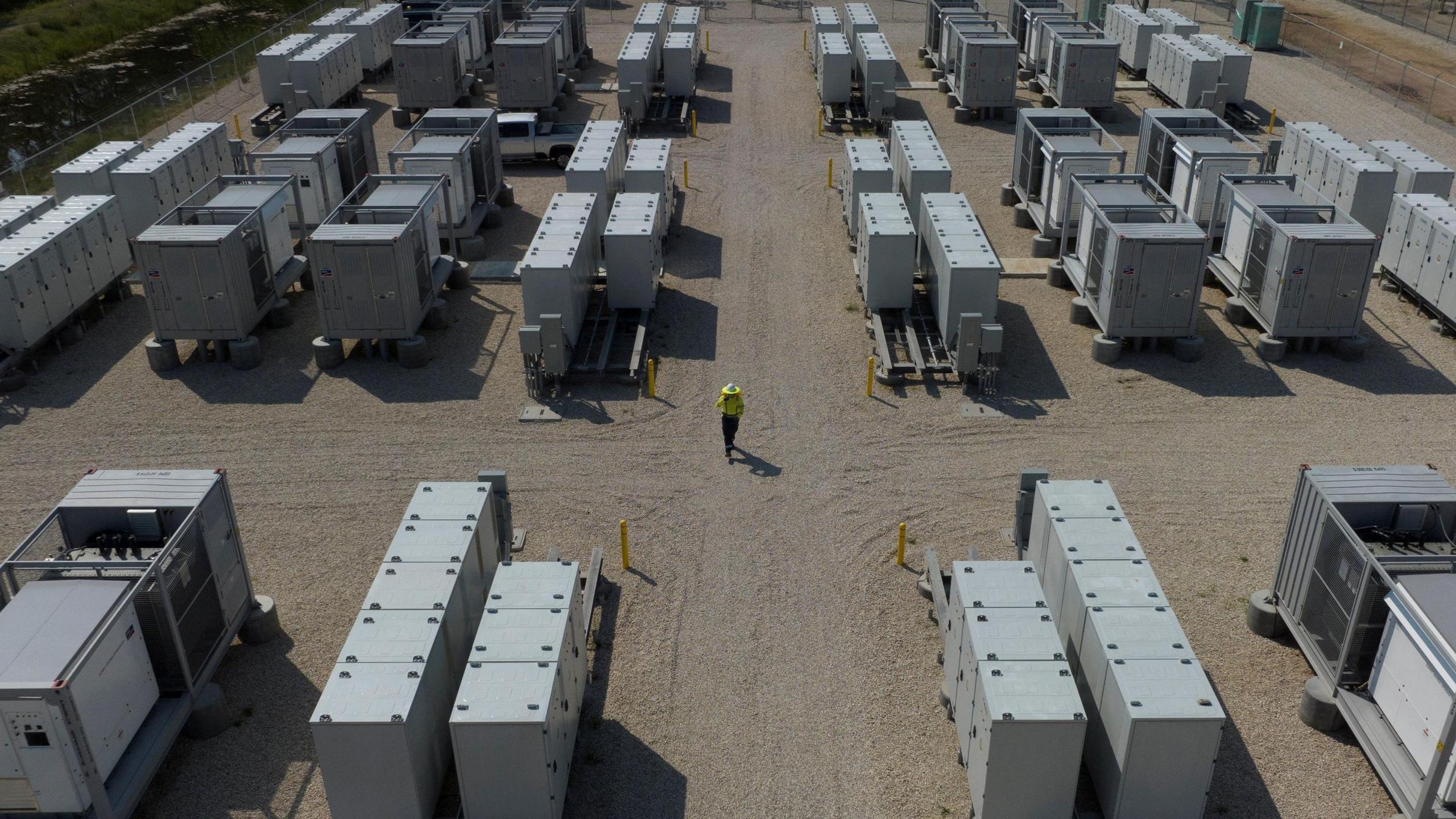 A drone view of a battery storage facility, with dozens of grey container sized units within a compound