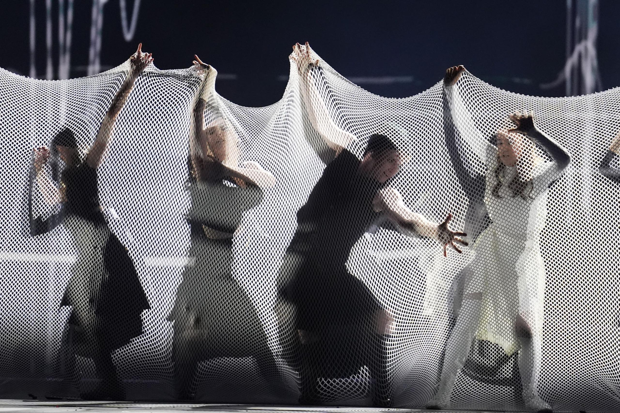 Dancers are covered in a tube of white mesh, they are reaching upwards and outwards to change the material's shape.