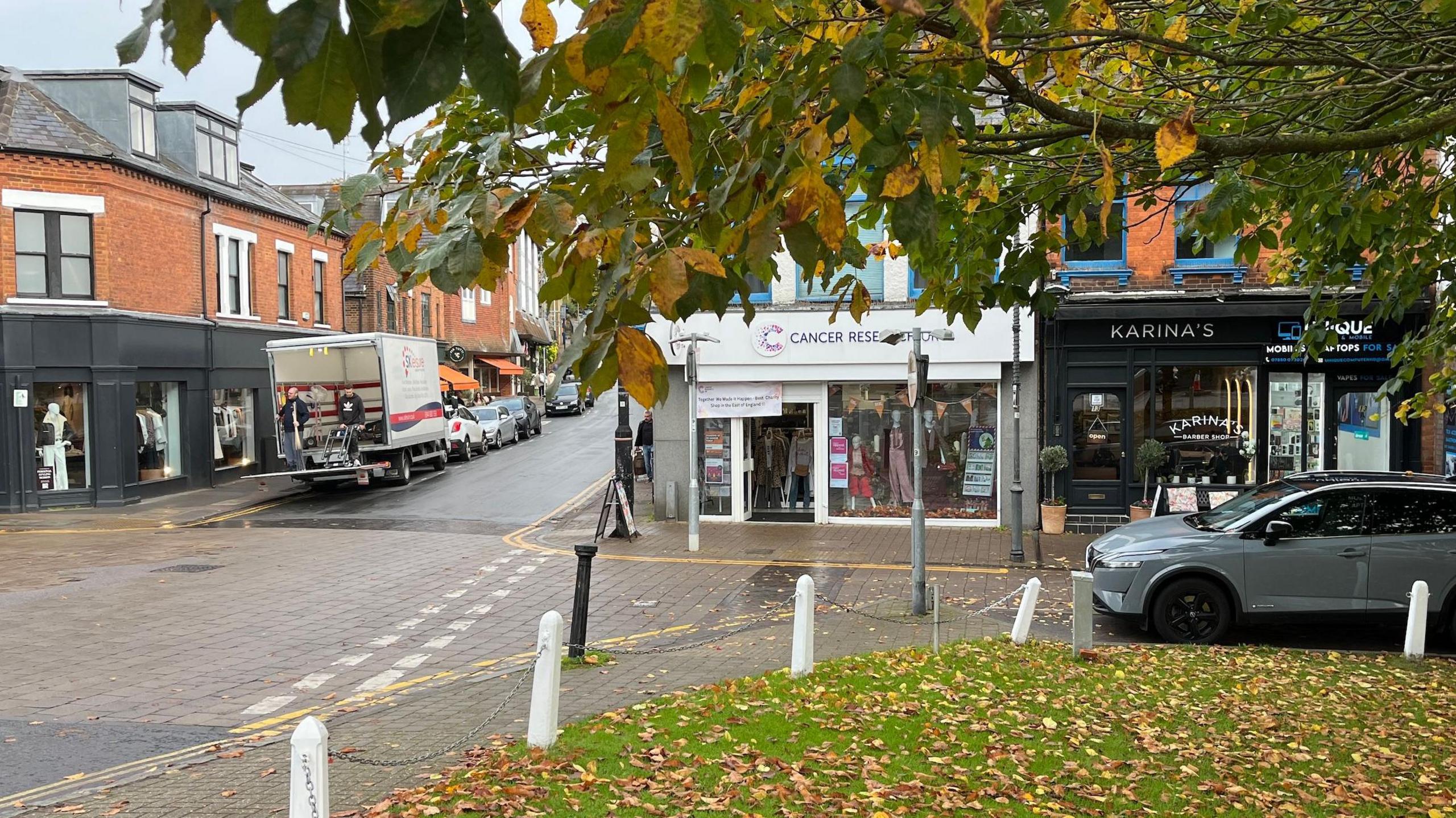 Cancer Research UK shop front next to a barber's shop on Harpenden high street.