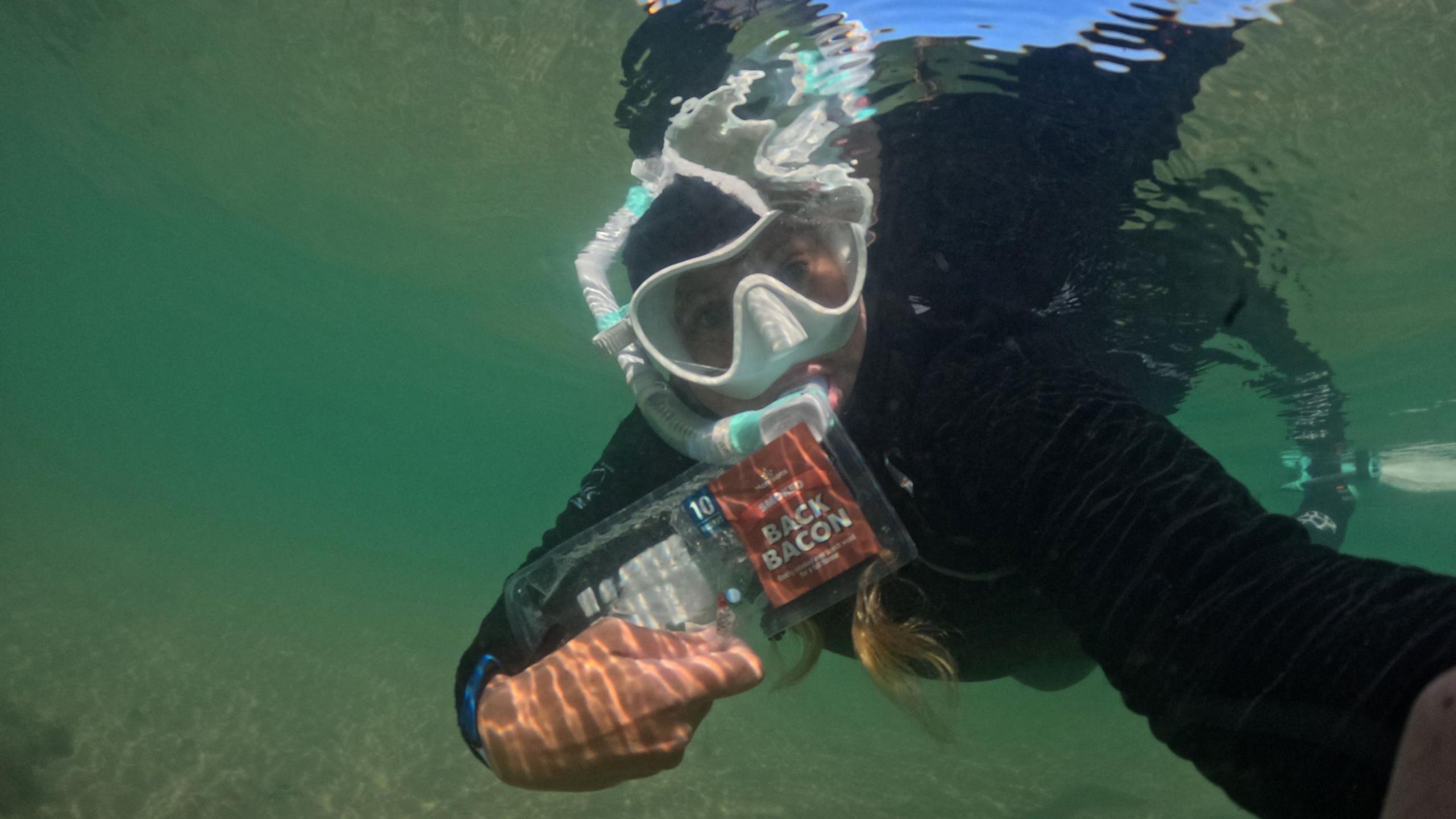 Maria underwater with an empty packet of bacon litter