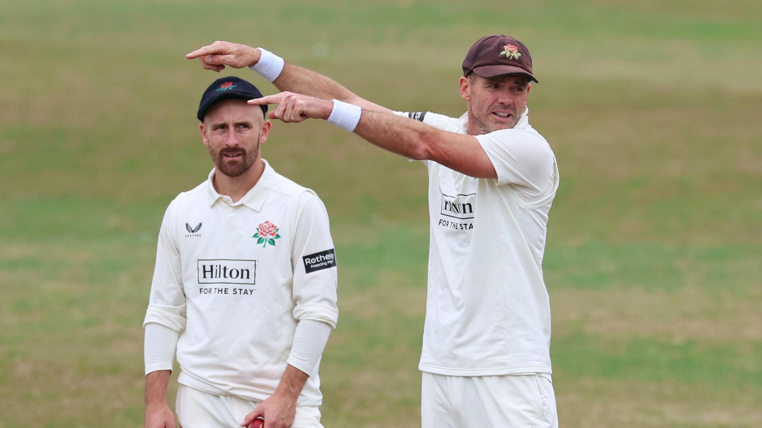 Josh Bohannon (left) watches as Sir James Anderson points to the right with both arms, passing instructions in the field to Lancashire players
