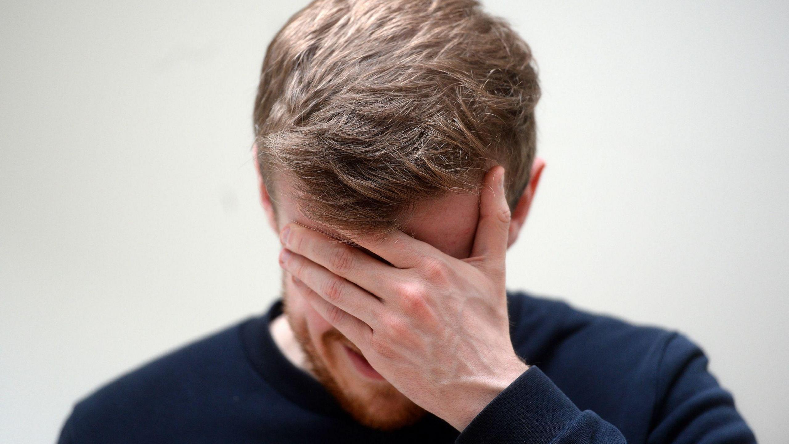 A man holding his head in his hands. He has a ginger beard and his hand is covering a majority of his face.