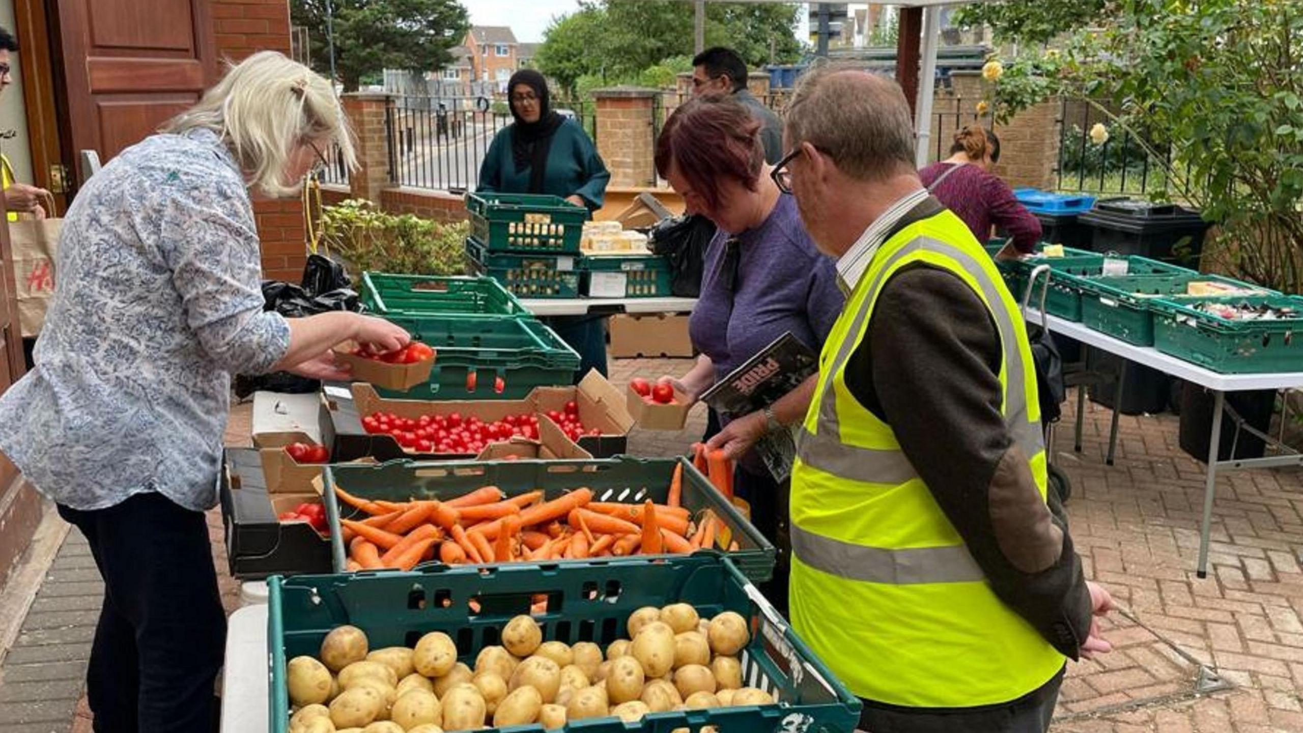 Staff at London's Community Kitchen sort piles of red tomatoes, orange carrots and potatoes into green trays on trestle tables