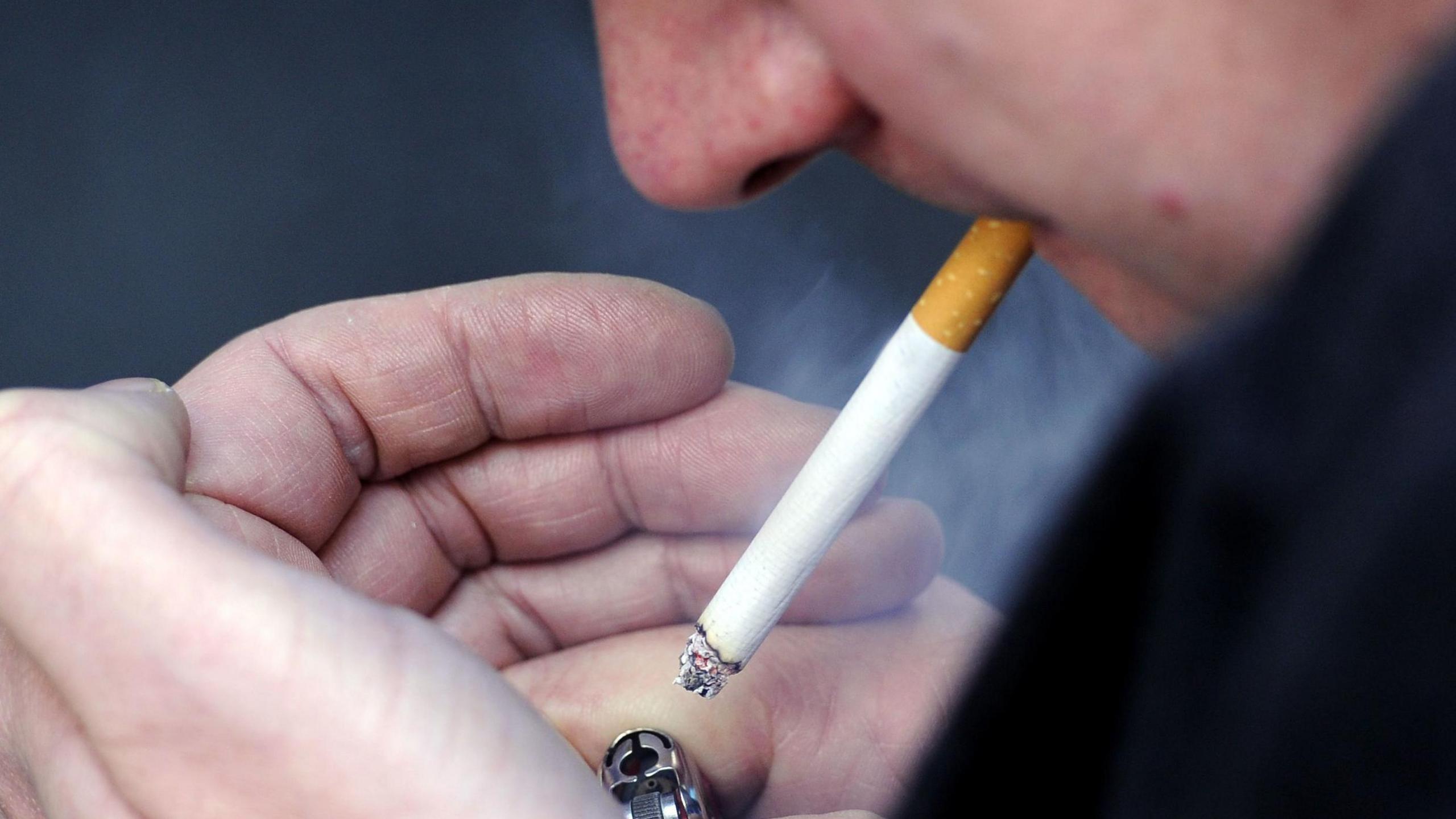 Llun agos o wyneb dyn yn tanio sigaret