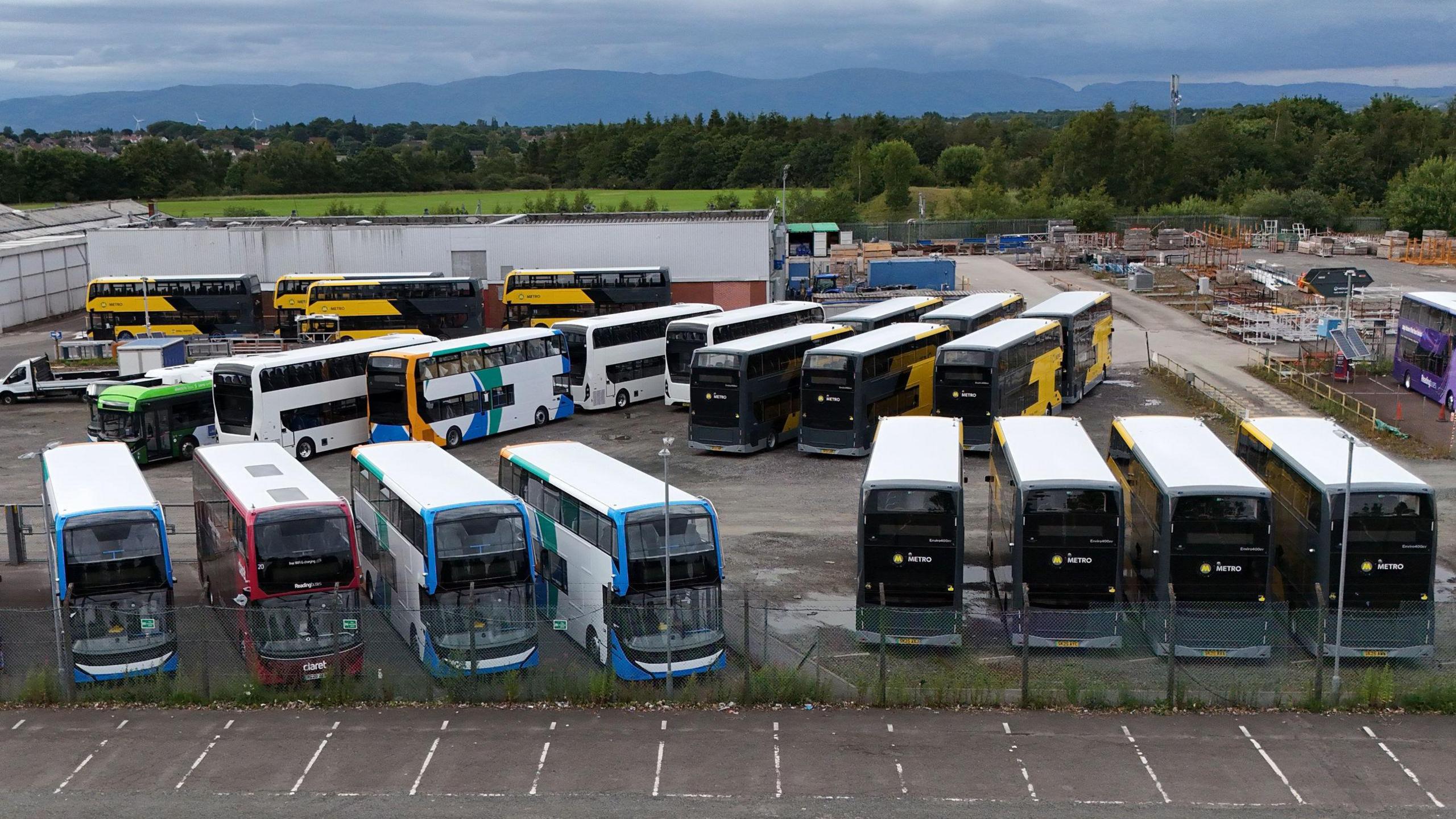 A lot of double decker buses parked outside at a manufacturing warehouse.