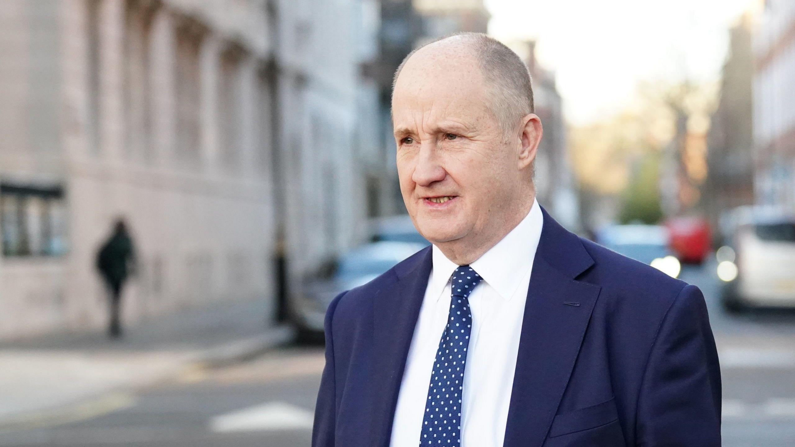 File image of Kevin Hollinrake, a man wearing a navy blue suit, white shirt and navy blue patterned tie, walking along a street